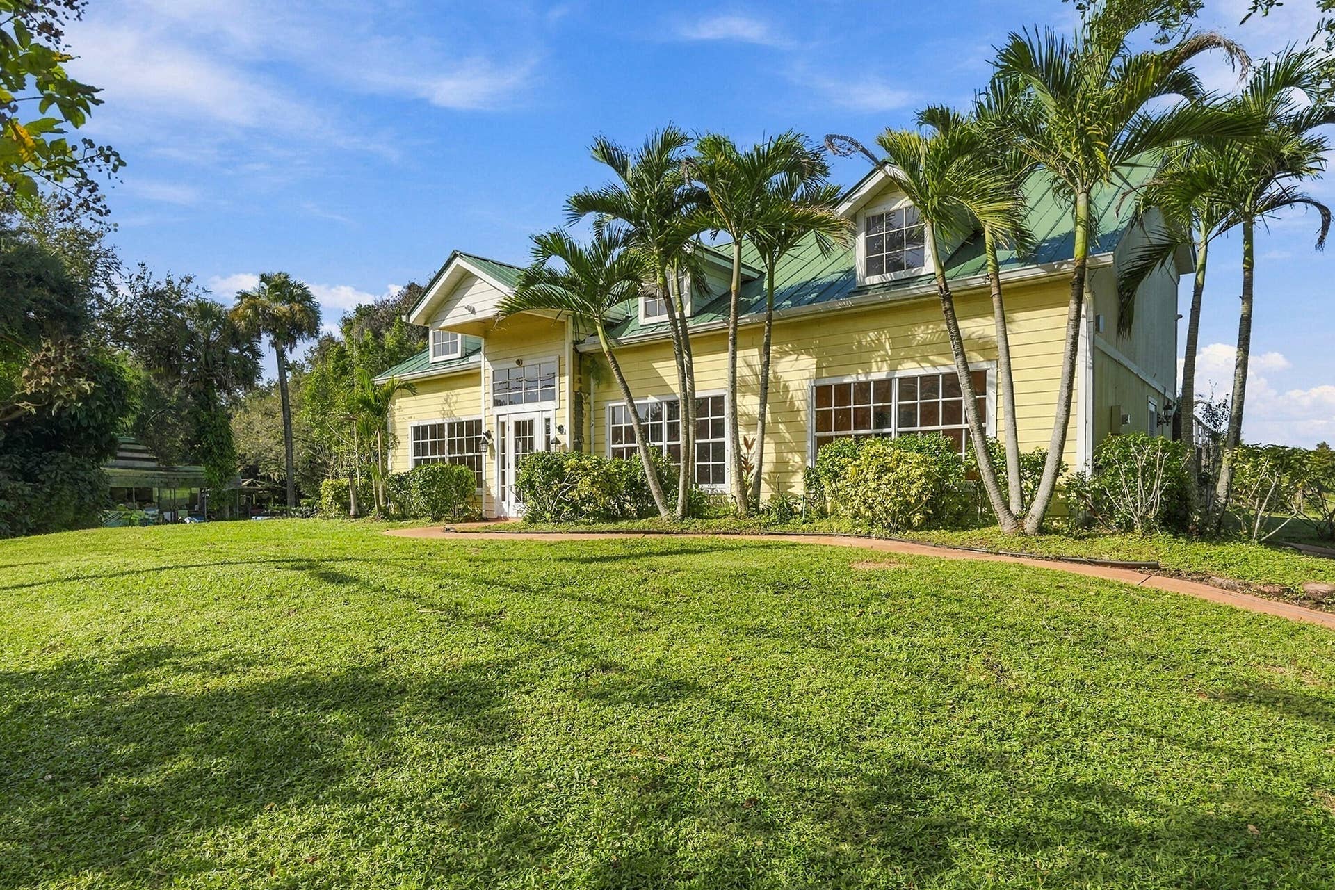 Exterior featuring yellow horizontal lap siding, a pitched green metal roof, multiple dormer windows, large multi-pane windows, and a paved walkway