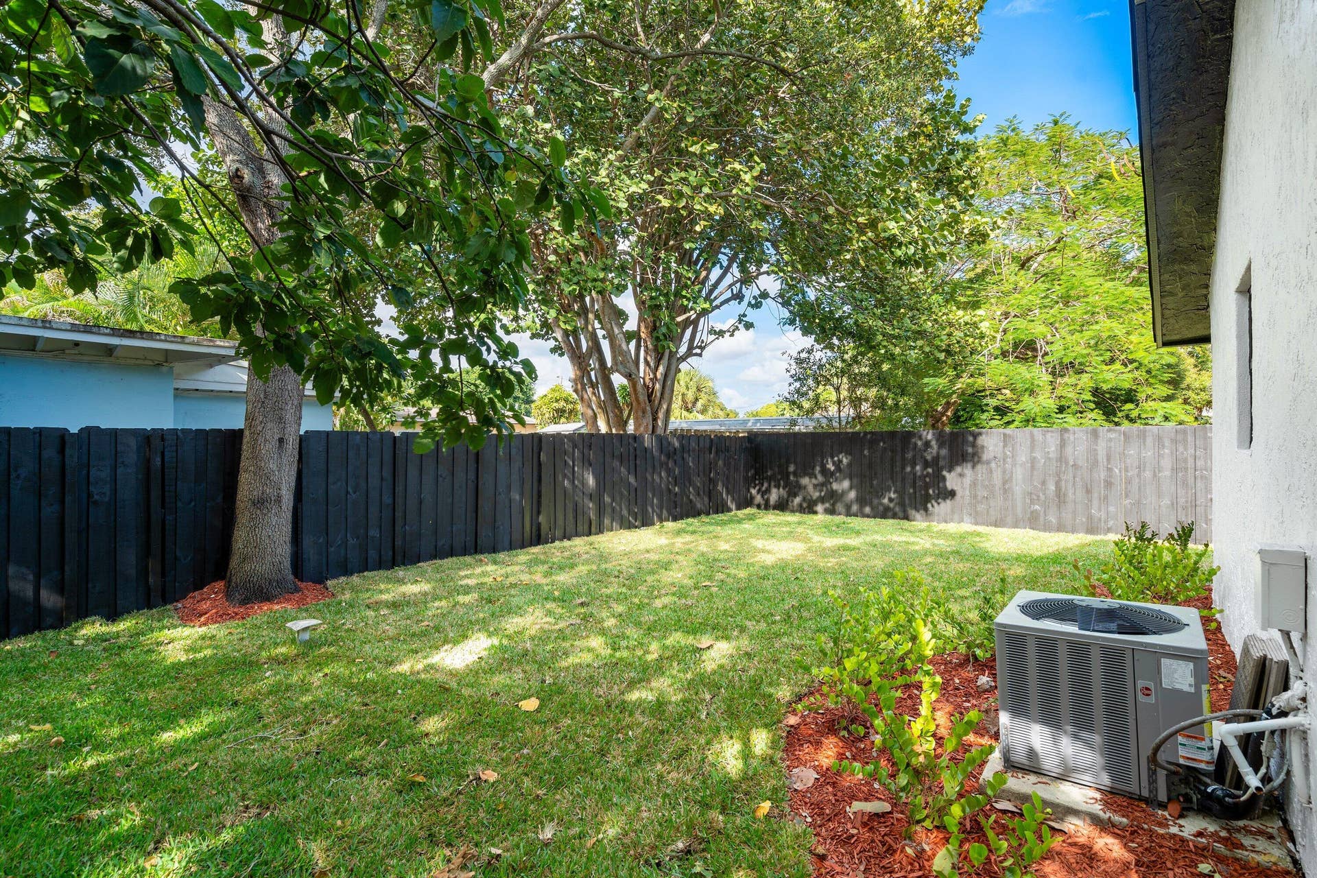 1211 NE 2nd Avenue, Fort Lauderdale, FL 33304 Backyard featuring a manicured lawn, perimeter wood fencing, established trees, and organic mulch landscaping