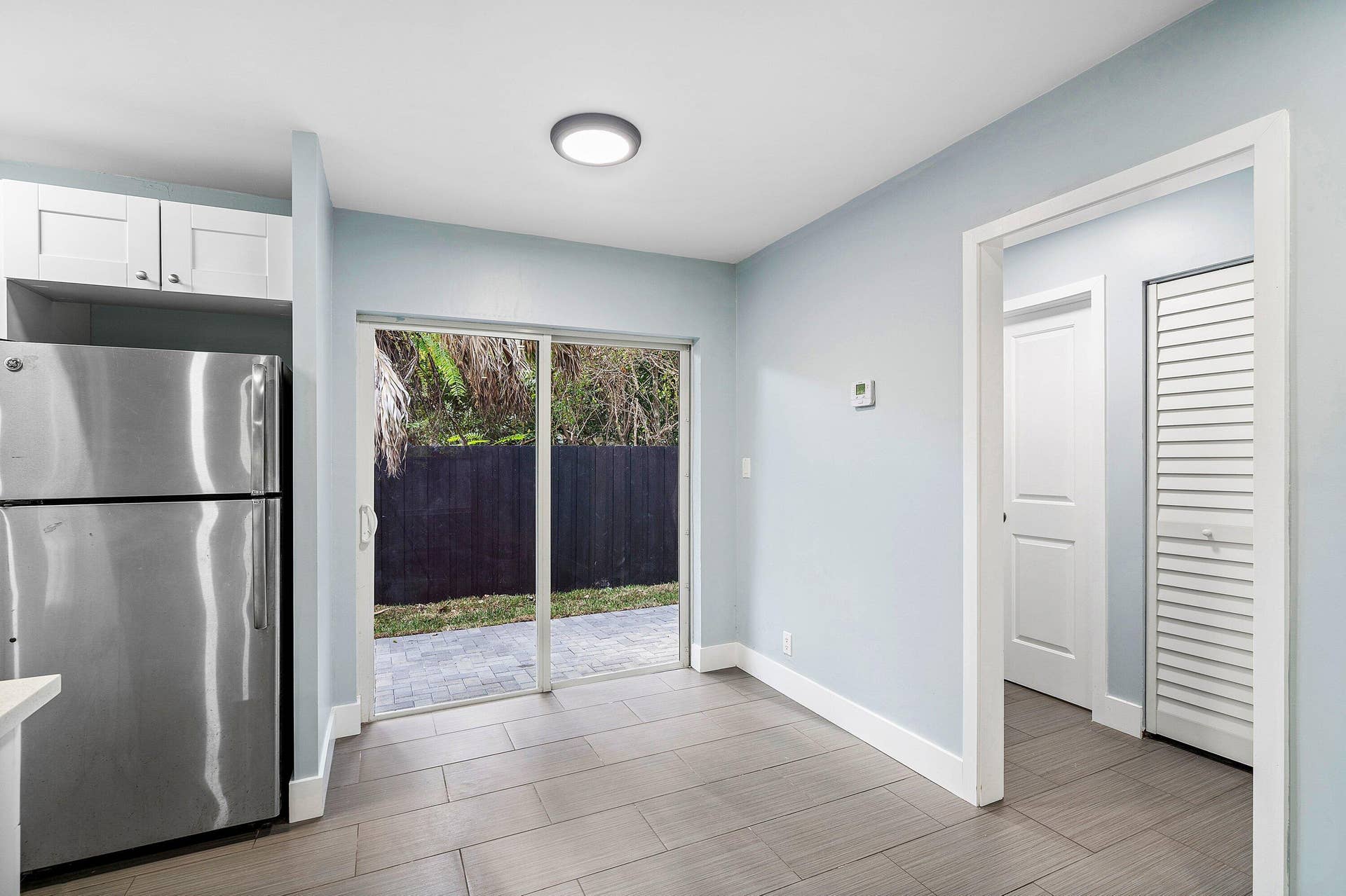 1211 NE 2nd Avenue, Fort Lauderdale, FL 33304 Kitchen space featuring white shaker-style cabinetry, stainless steel refrigerator, tile flooring, and sliding glass doors leading to a paved patio
