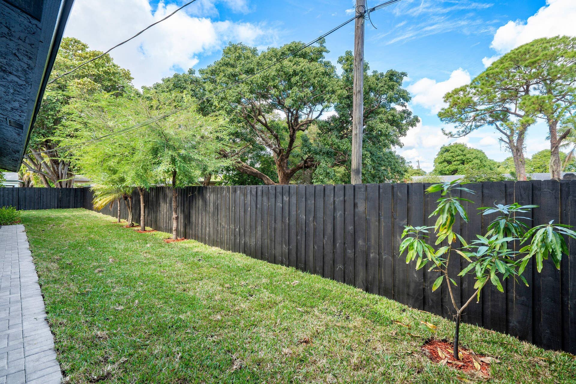 1211 NE 2nd Avenue, Fort Lauderdale, FL 33304 Private backyard featuring a paved stone walkway, perimeter dark-stained vertical wood fencing, manicured lawn, and mature canopy trees