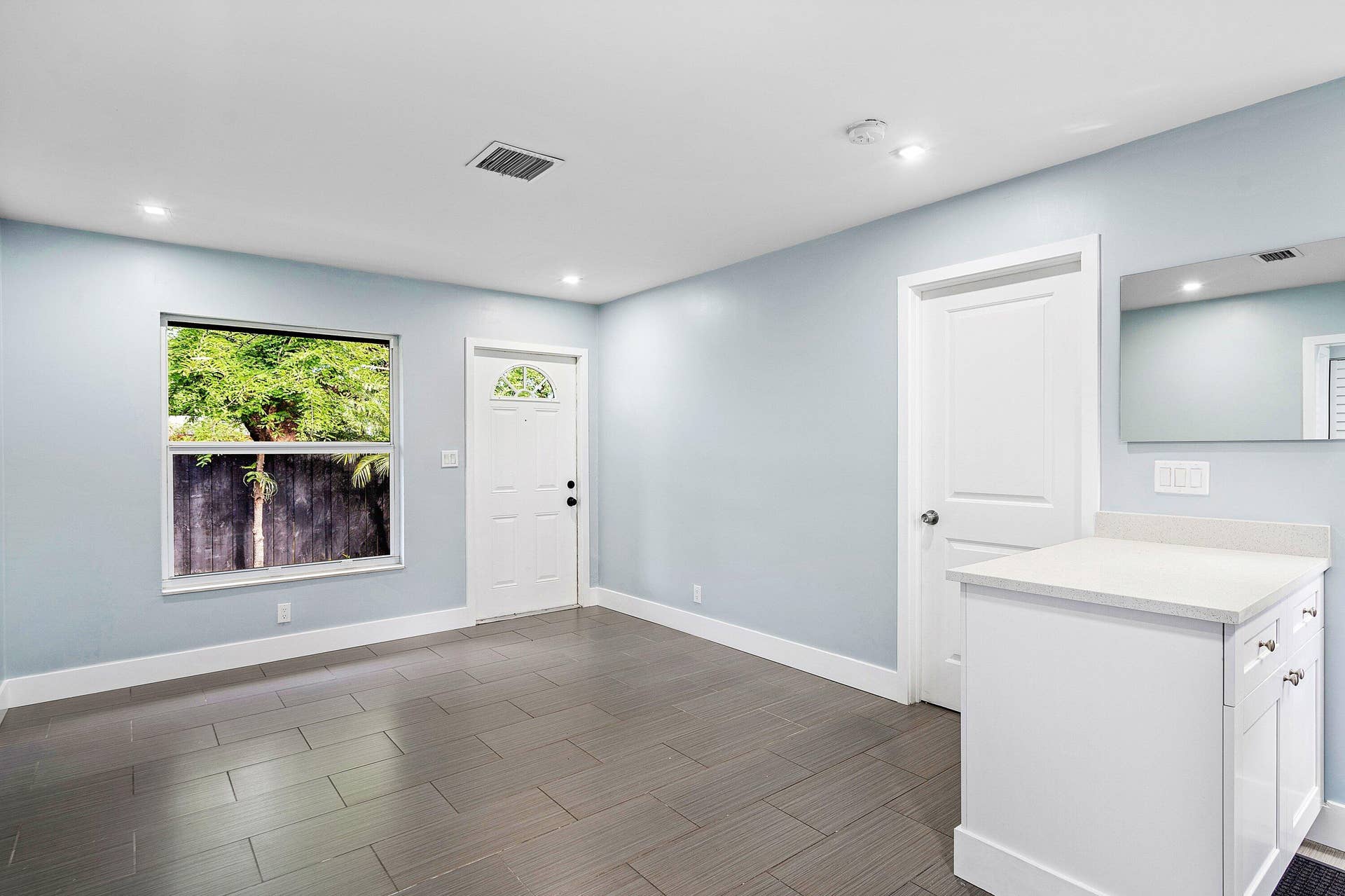1211 NE 2nd Avenue, Fort Lauderdale, FL 33304 Neutral-toned interior featuring large-format rectangular floor tile, recessed lighting, white built-in cabinetry with a stone-surface countertop, and a single-hung window