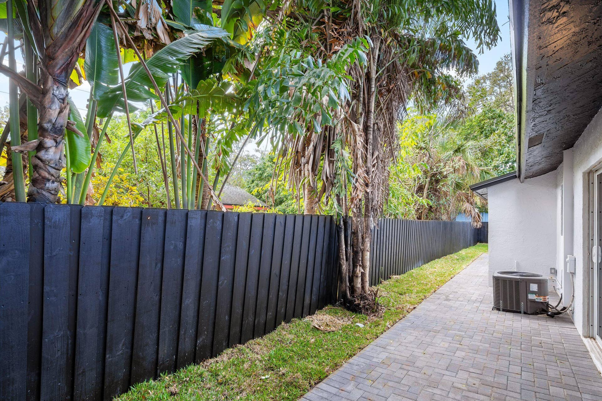 1211 NE 2nd Avenue, Fort Lauderdale, FL 33304 Side yard featuring a paver stone patio, a dark wood-finish privacy fence, and mature palm trees