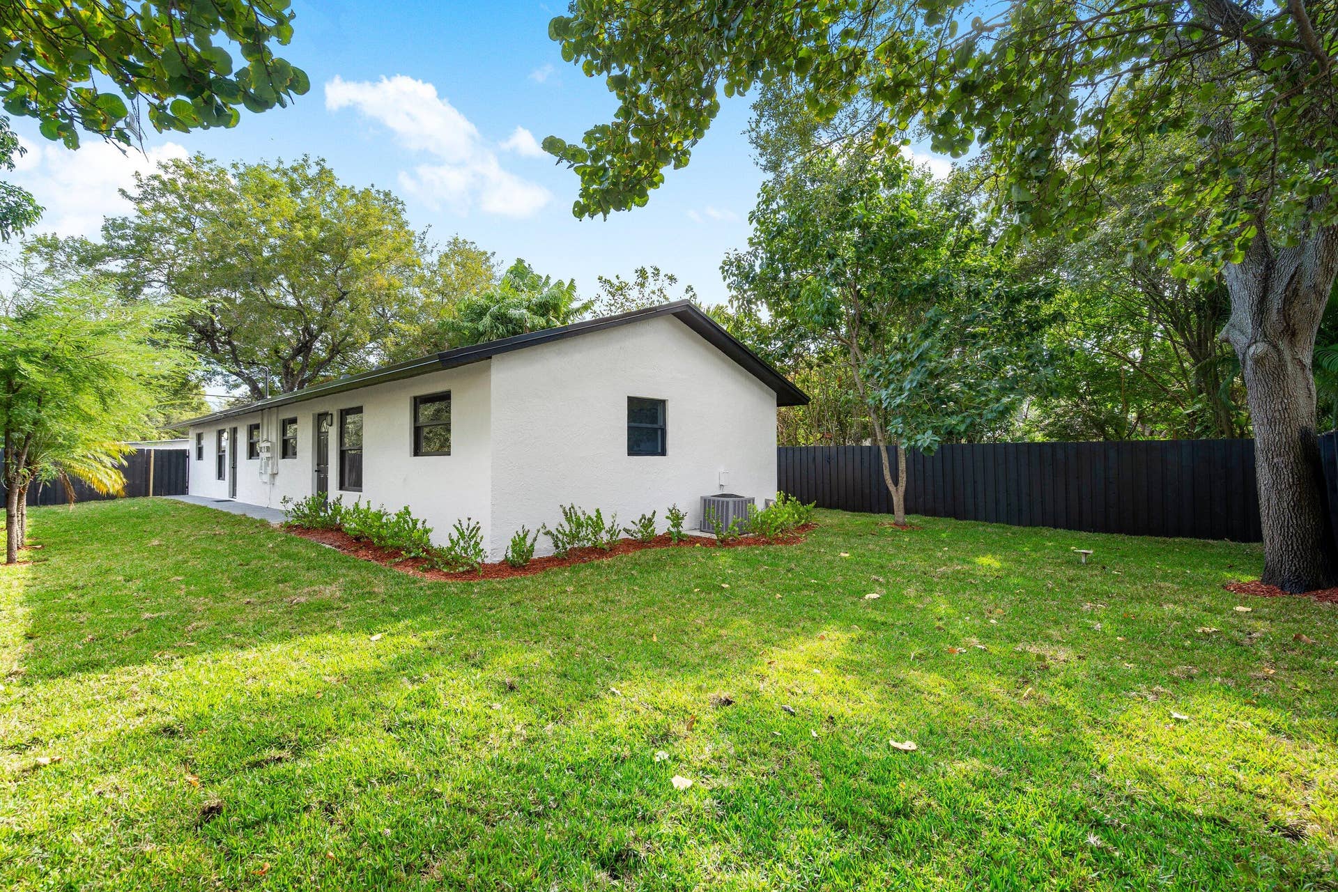 1211 NE 2nd Avenue, Fort Lauderdale, FL 33304 Rear exterior featuring white stucco siding, dark trim, manicured lawn, and black perimeter fencing