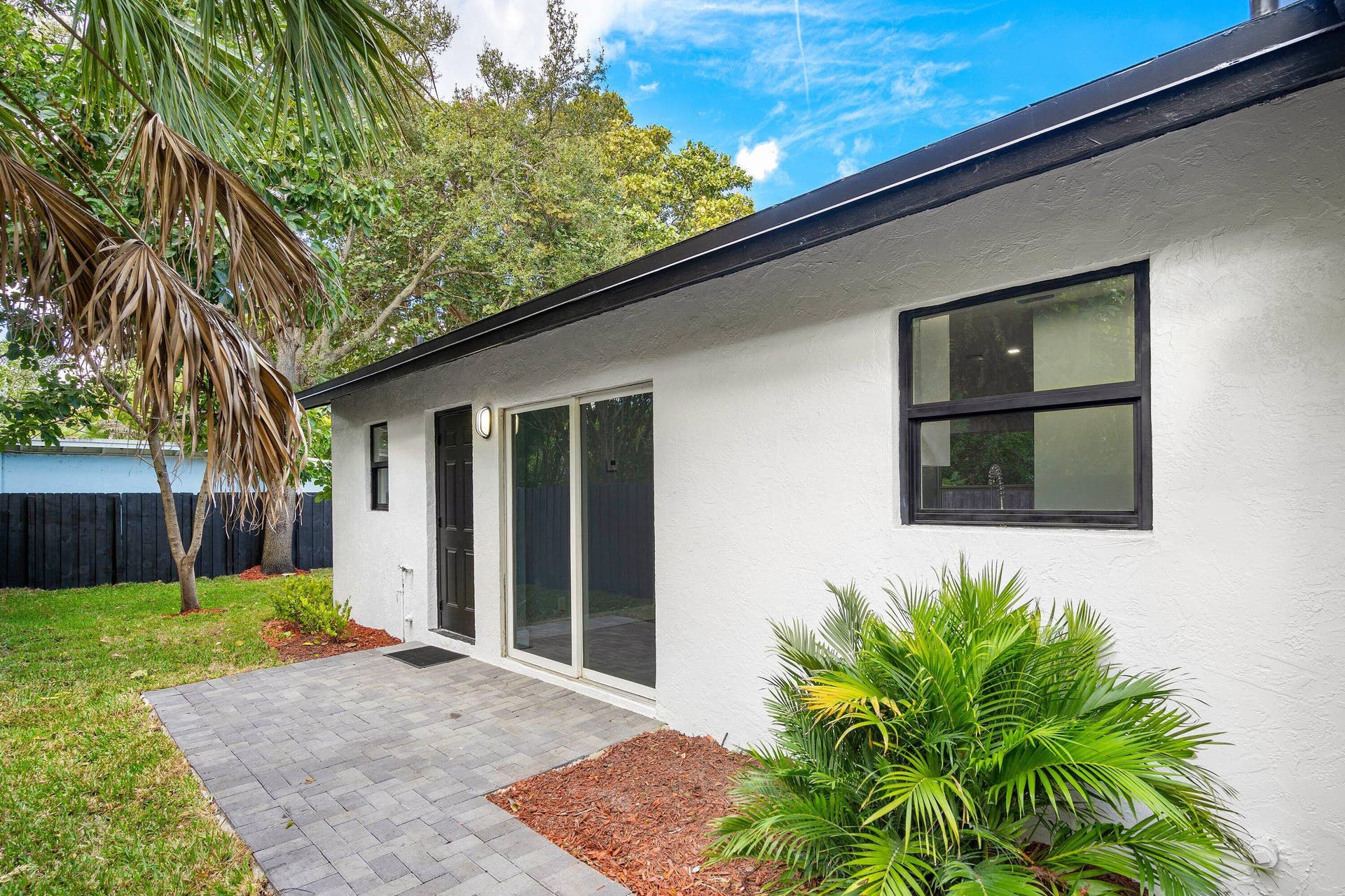 1211 NE 2nd Avenue, Fort Lauderdale, FL 33304 Stucco exterior featuring sliding glass doors, a paver patio, dark-finished window frames, and exterior wall-mounted lighting