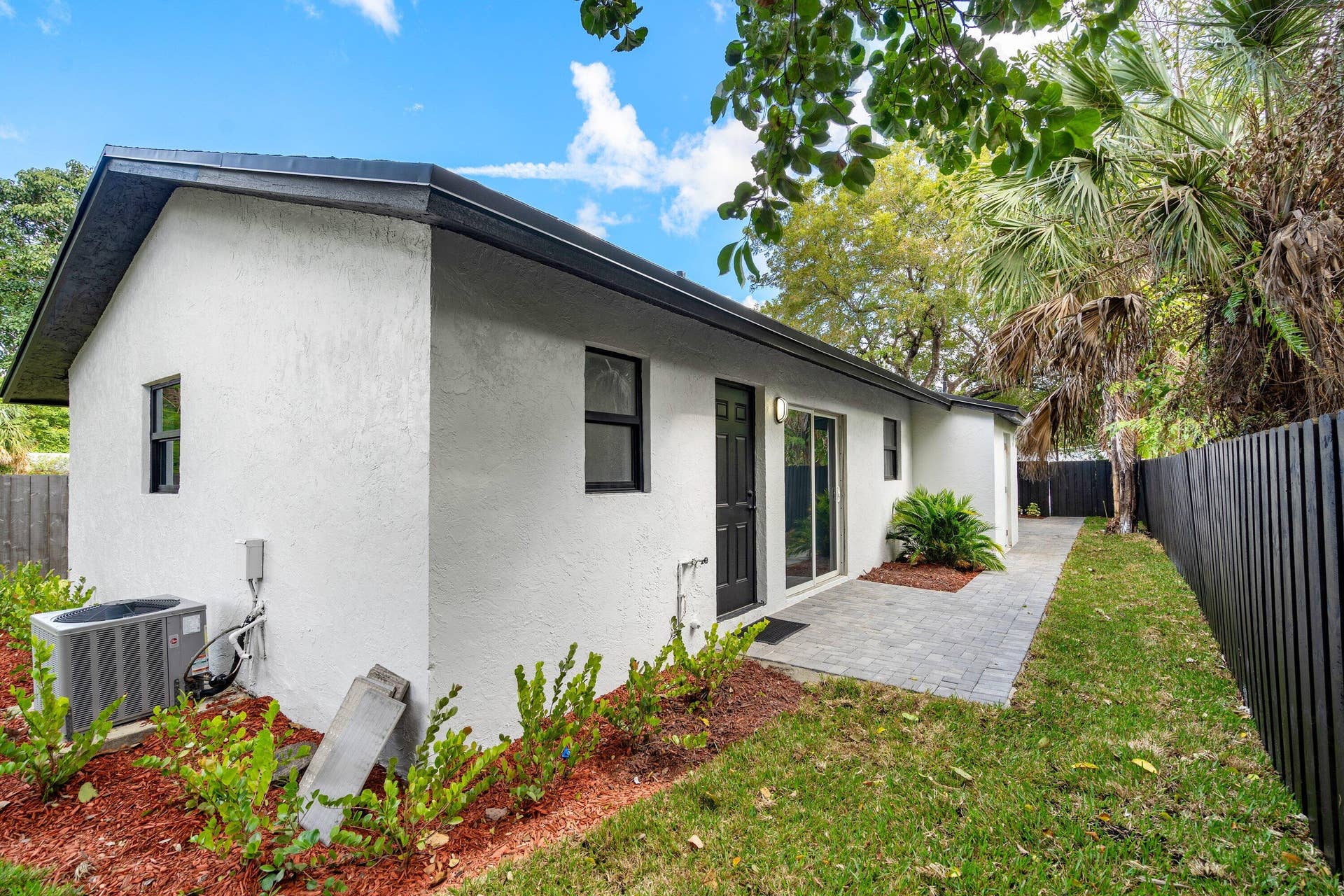 1211 NE 2nd Avenue, Fort Lauderdale, FL 33304 Stucco exterior featuring a paver patio, sliding glass door, and dark-toned privacy fencing