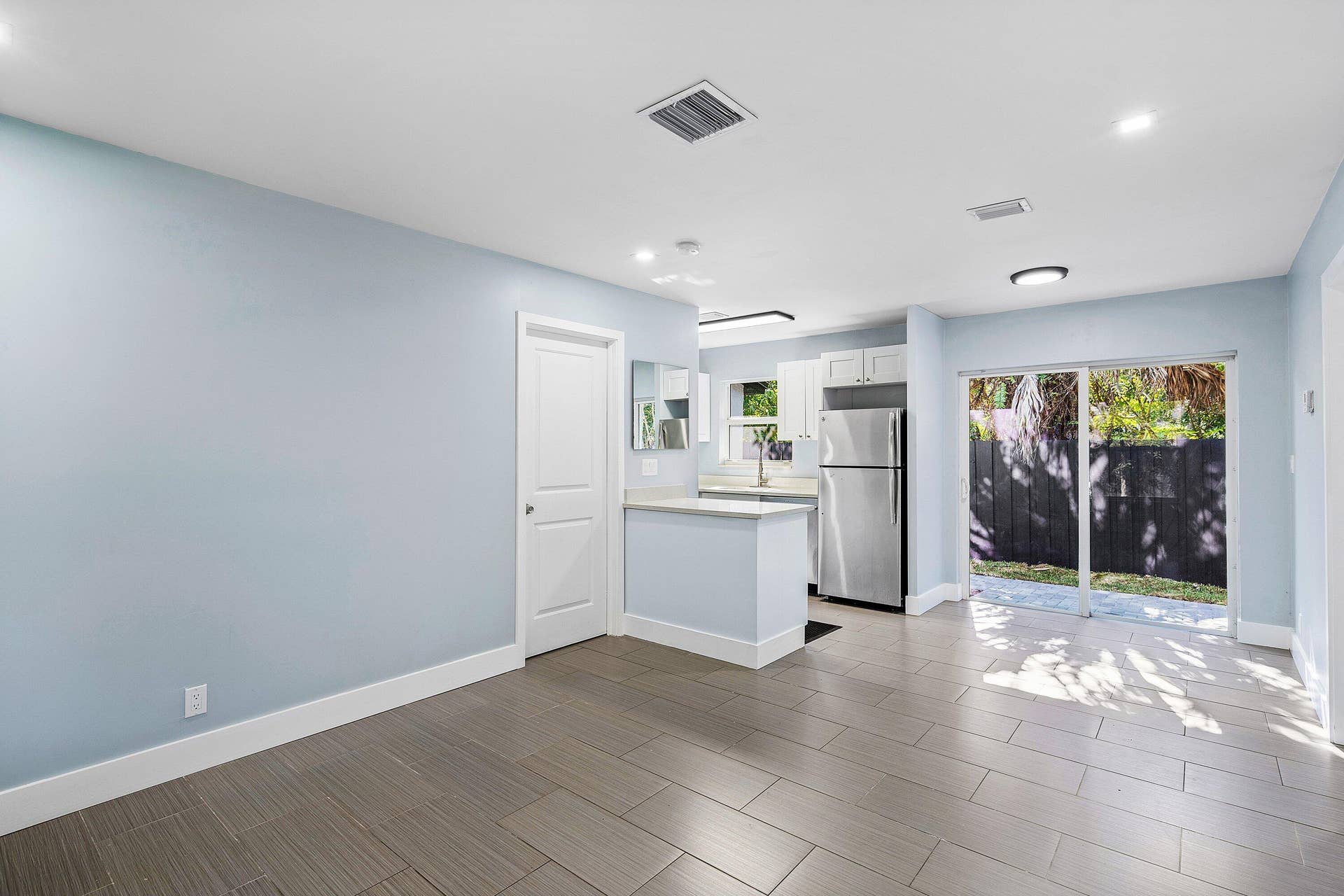 1211 NE 2nd Avenue, Fort Lauderdale, FL 33304 Open-concept interior featuring large-format tile flooring, kitchen with stainless steel refrigerator, white cabinetry, solid-surface countertops, and sliding glass doors