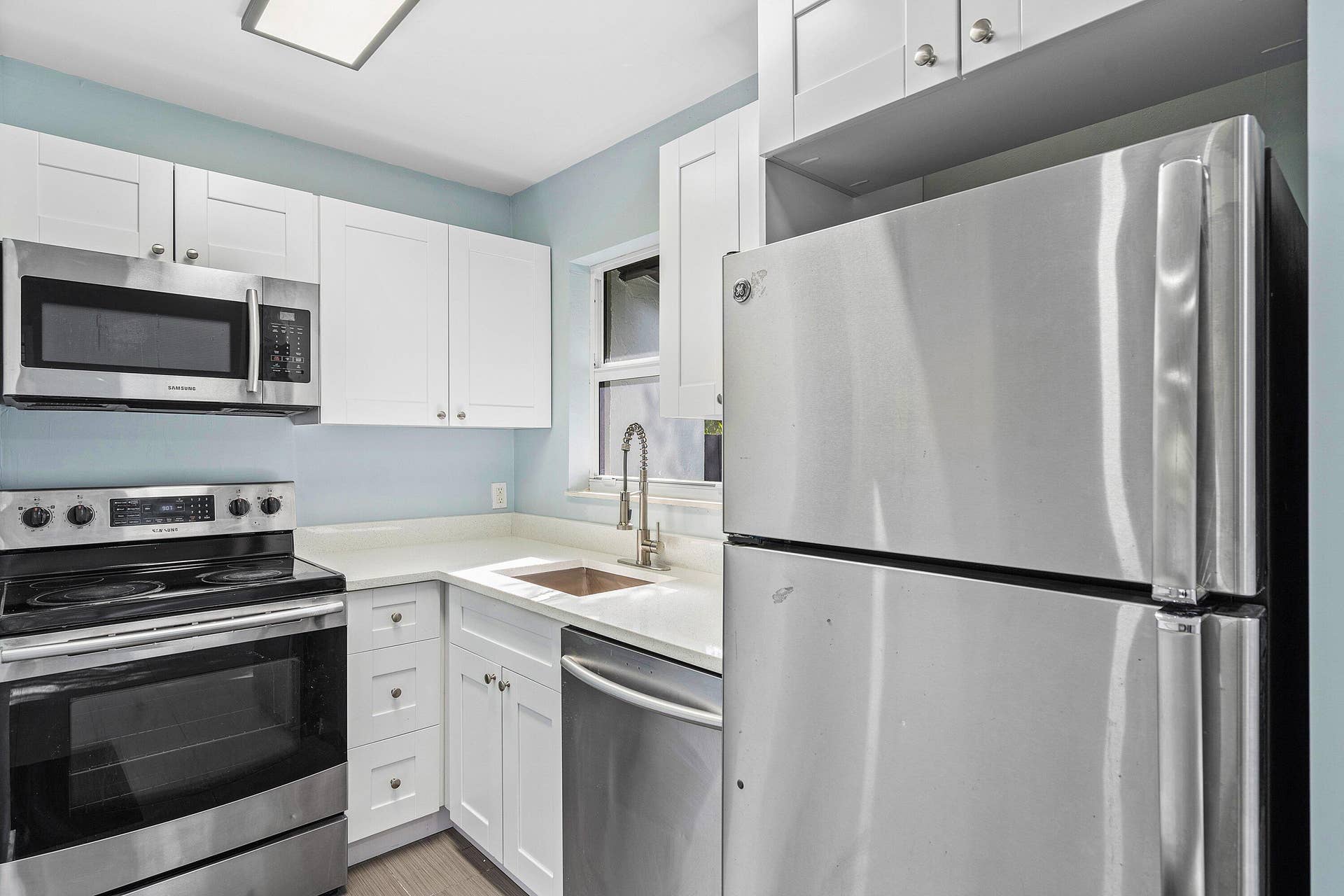 1211 NE 2nd Avenue, Fort Lauderdale, FL 33304 Kitchen featuring white shaker-style cabinetry, solid-surface countertops, stainless steel appliances, and a gooseneck faucet