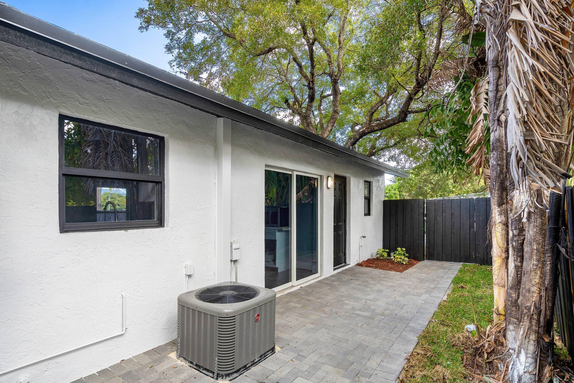 1211 NE 2nd Avenue, Fort Lauderdale, FL 33304 Stucco exterior featuring sliding glass doors, paver patio, and dark wood-tone privacy fencing