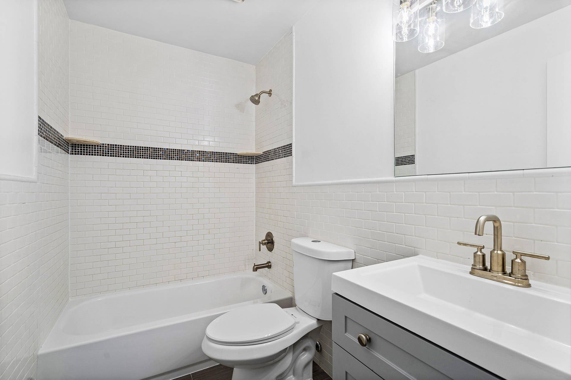 1211 NE 2nd Avenue, Fort Lauderdale, FL 33304 Bathroom featuring white subway tile walls with a mosaic tile inlay, a soaking tub with a wall-mounted showerhead, a grey vanity with a rectangular integrated sink, and metallic finish plumbing fixtures