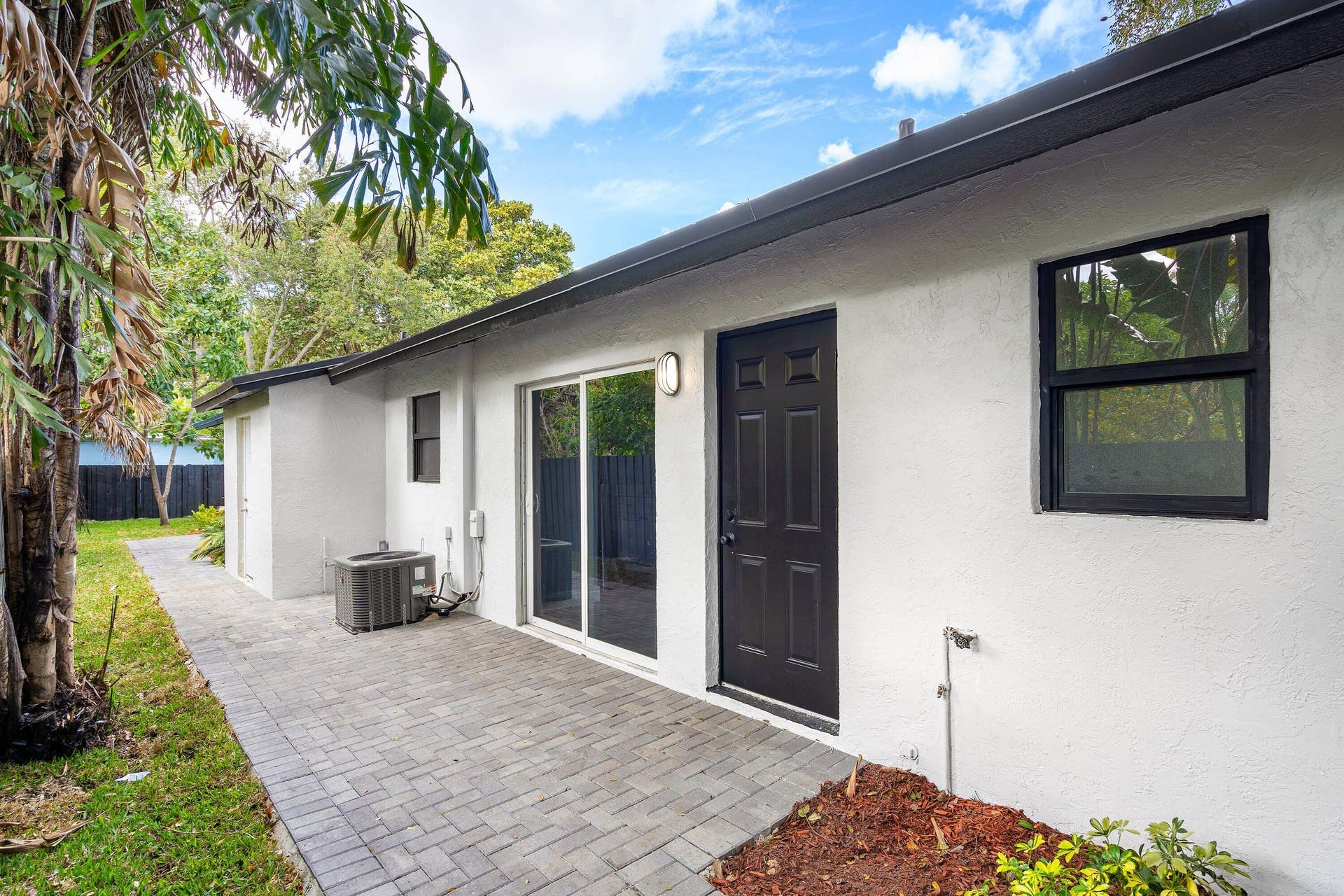 1211 NE 2nd Avenue, Fort Lauderdale, FL 33304 Exterior featuring a paved brick patio, white stucco finish, sliding glass door, and dark-trimmed windows