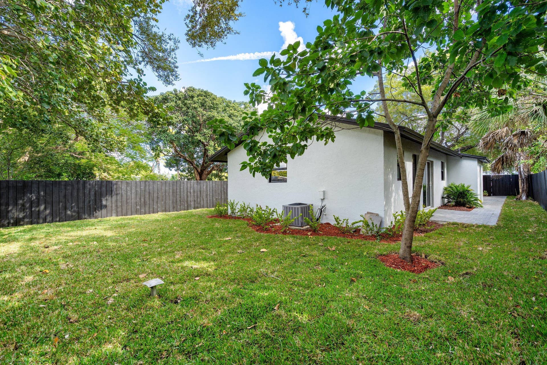 1211 NE 2nd Avenue, Fort Lauderdale, FL 33304 Spacious backyard with manicured lawn, perimeter wood fencing, mature trees, landscaped mulch beds, and paved patio space