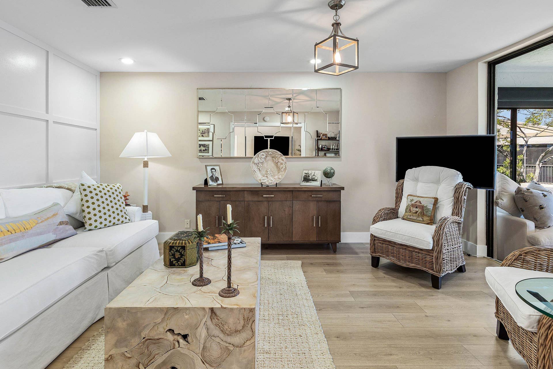 Living area featuring wood-finish flooring, grid-pattern wall molding, large decorative wall mirror, and modern geometric pendant lighting