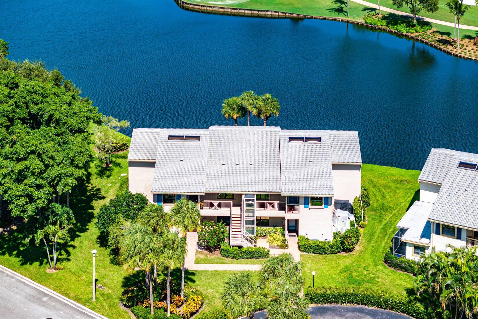 Multi-level building exterior featuring light-toned masonry, shingled roofing, balcony spaces, and waterfront positioning
