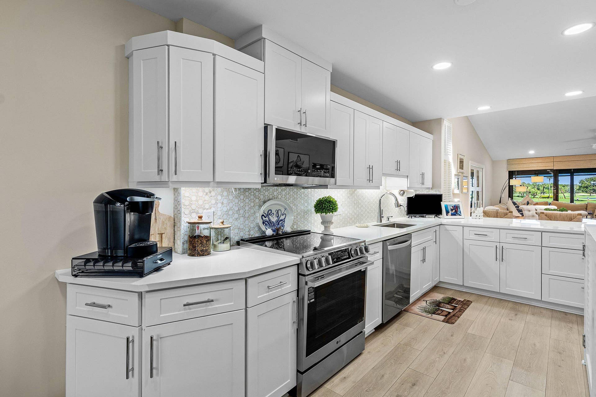 Kitchen featuring white Shaker-style cabinetry, quartz countertops, a patterned tile backsplash, stainless steel appliances, and wood-finish flooring