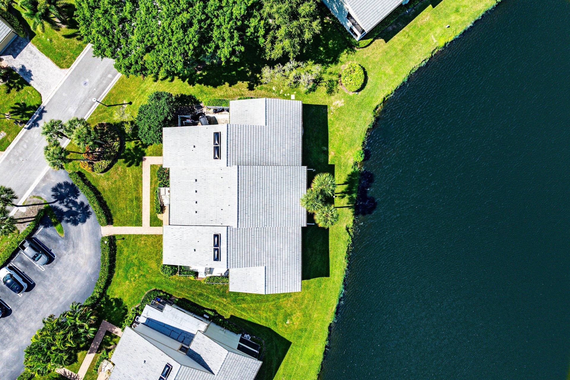 Aerial perspective featuring a tile roof, built-in skylights, waterfront positioning, and landscaped grounds