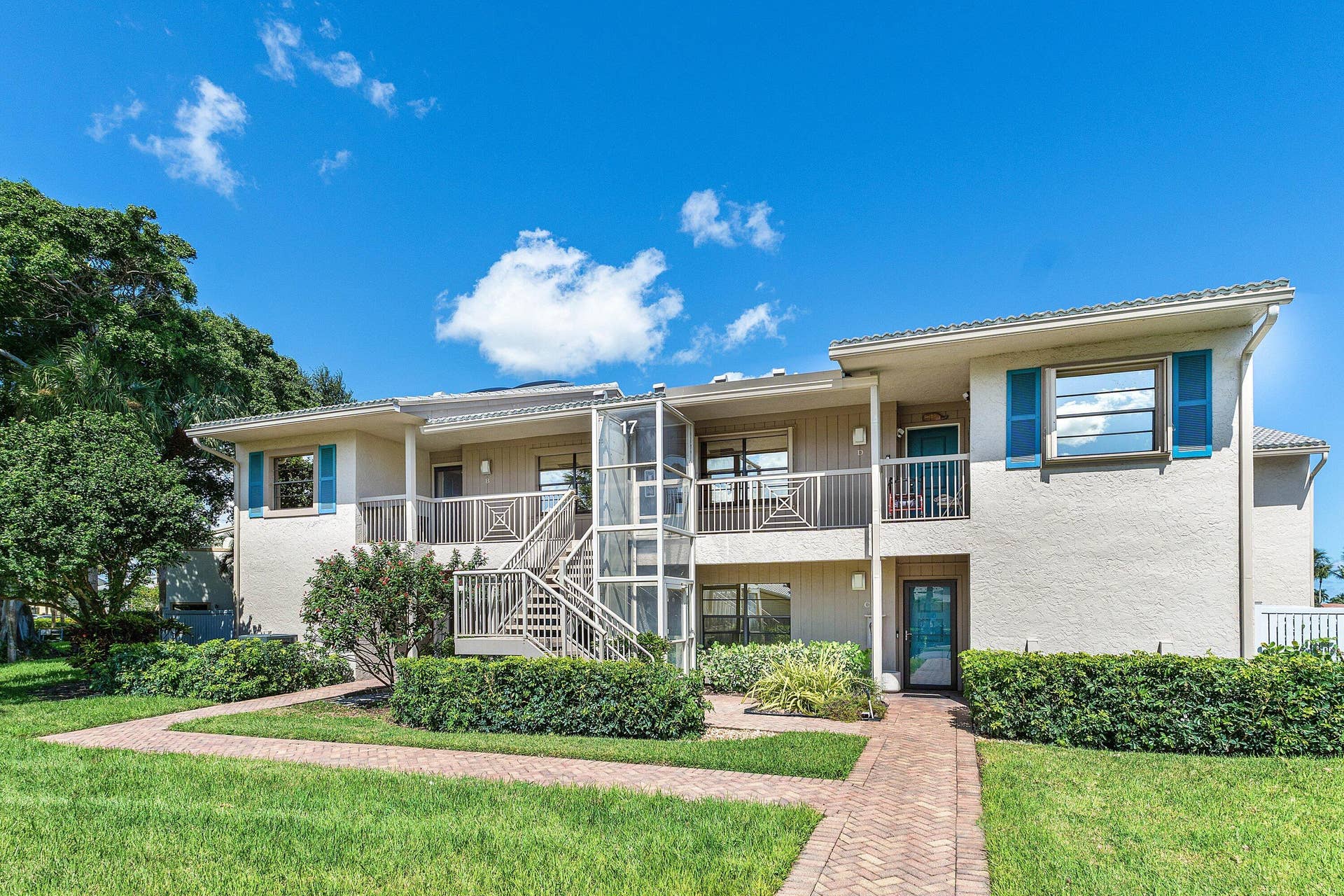 Exterior featuring stucco siding, metal staircase, glass-enclosed lift, second-level balcony with metal railing, and paver walkway