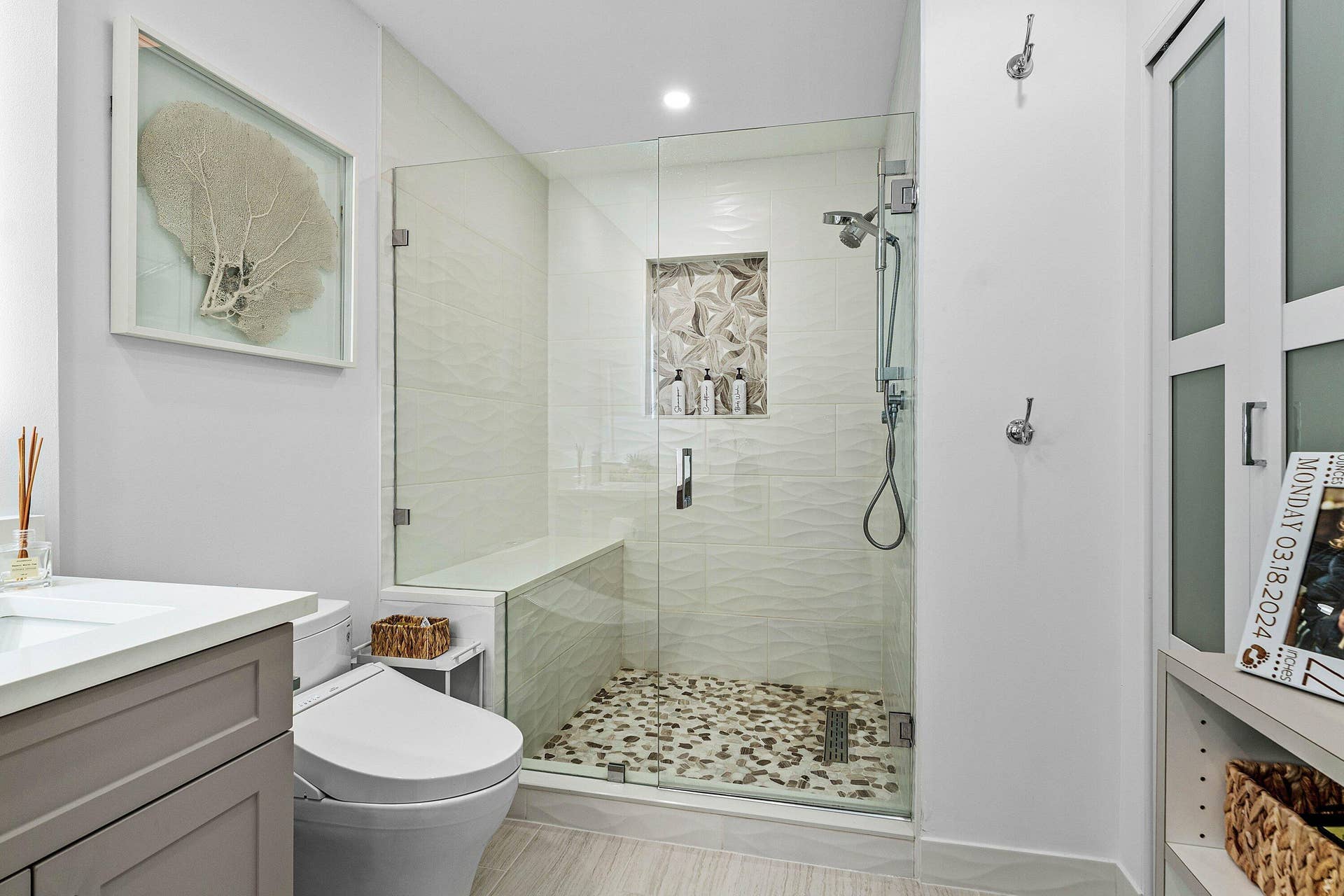 Walk-in shower featuring a frameless glass enclosure, pebble-stone flooring, built-in bench, and textured tile wall surround with a recessed niche