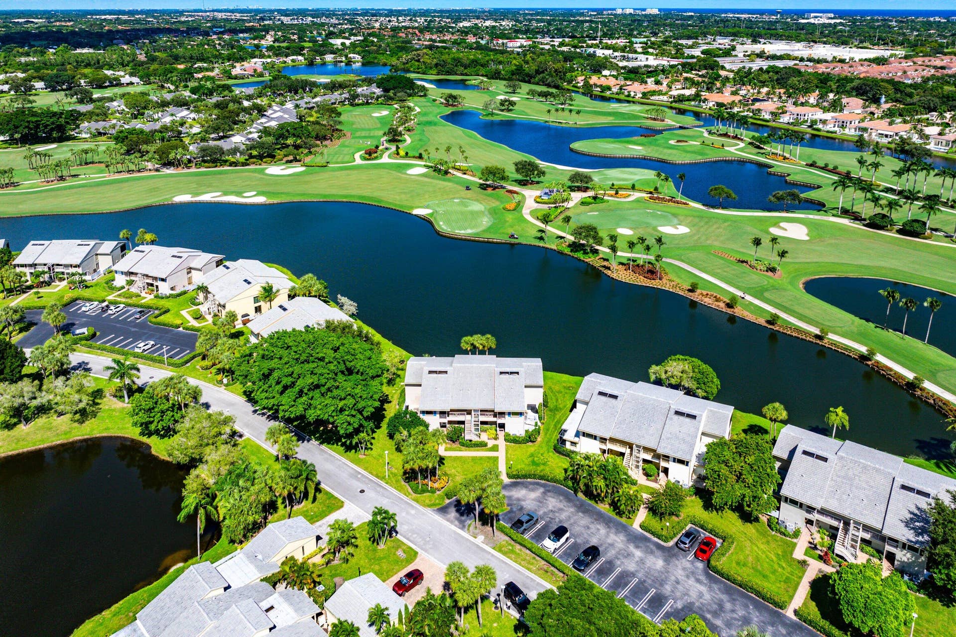 Aerial perspective featuring a golf course, expansive water features, manicured landscaping, and paved surface parking