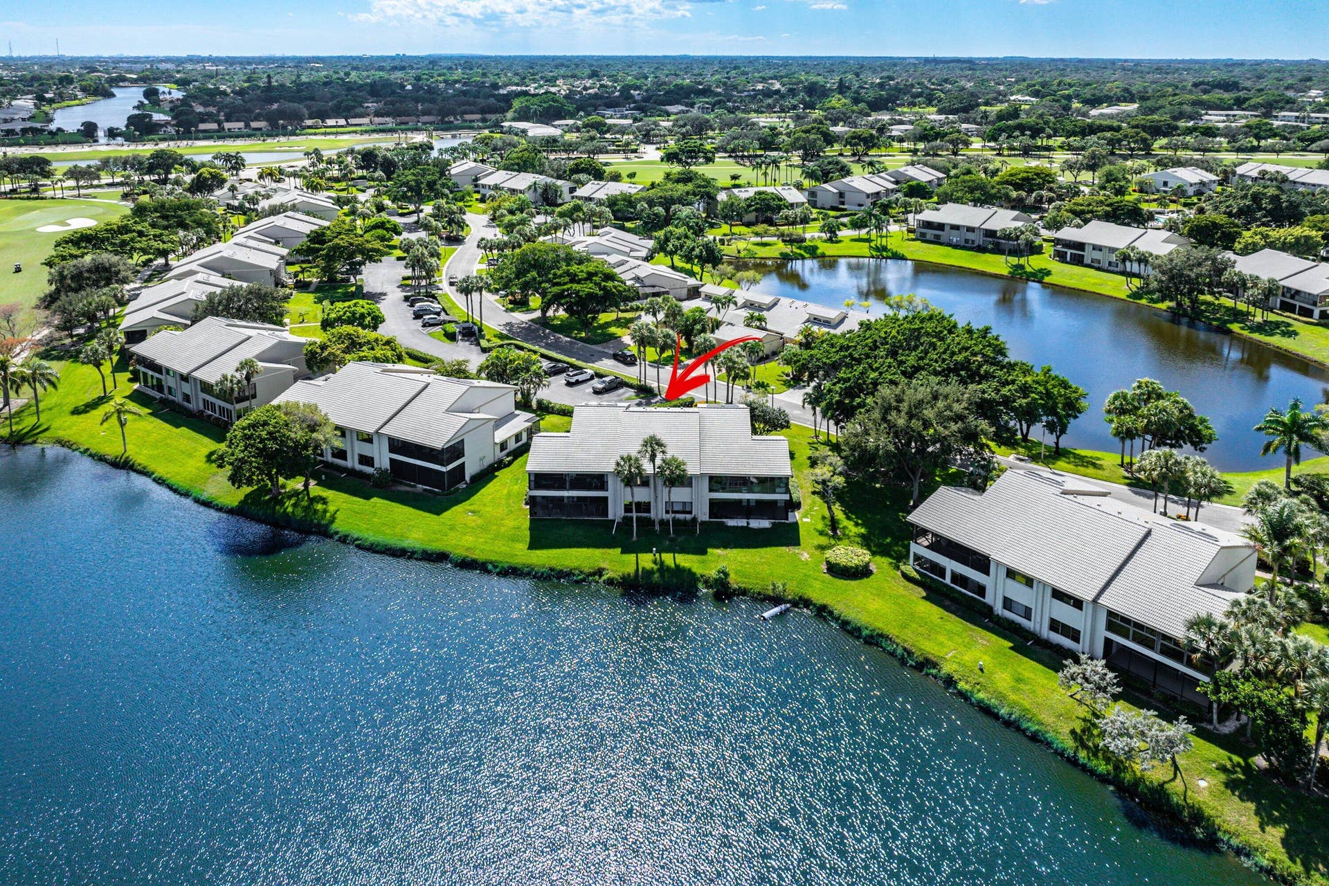 Aerial perspective of a multi-unit residential building featuring a tile roof, covered balconies, and waterfront positioning along a lake