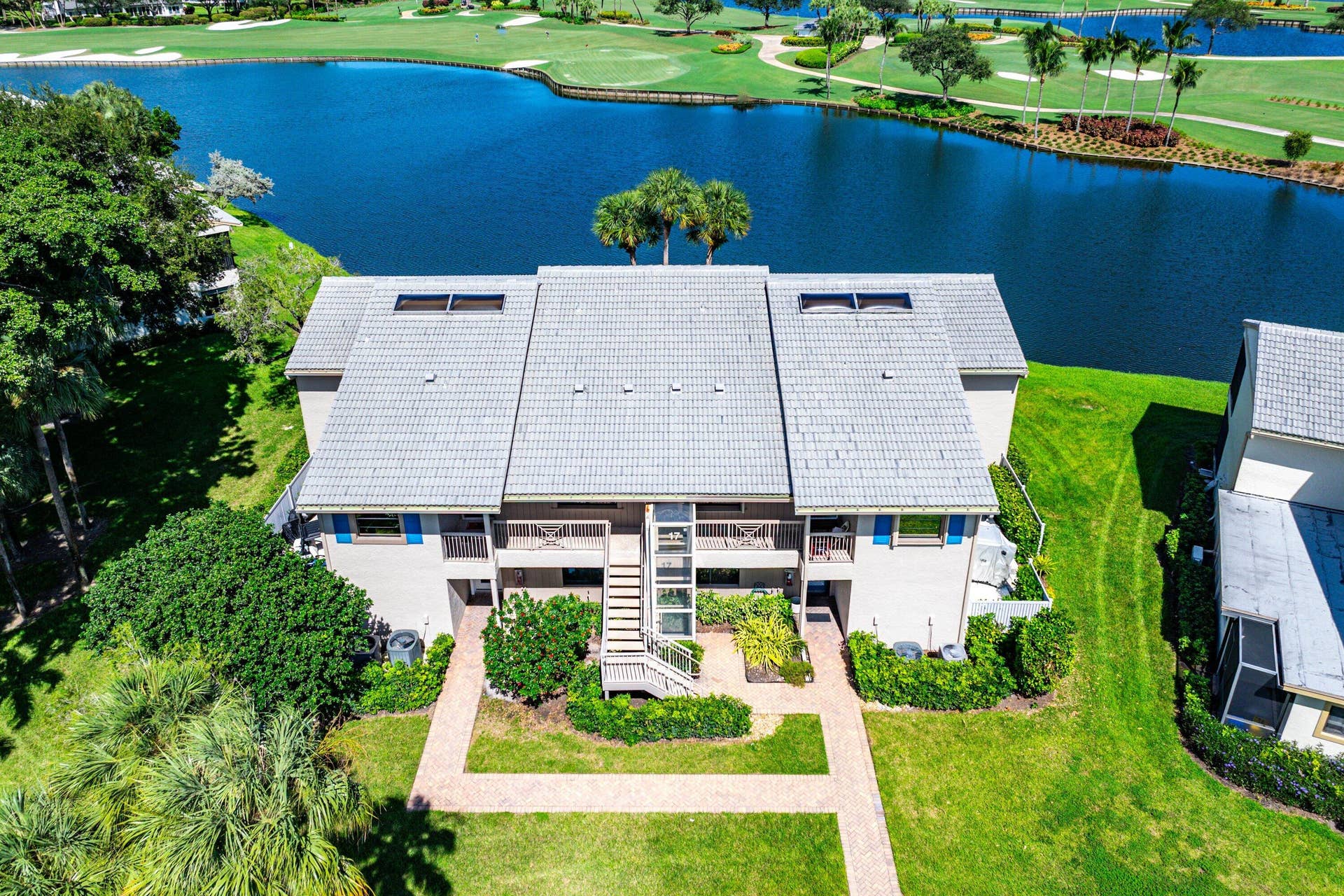 Aerial perspective of a multi-unit property featuring a tile roof, external staircases, stone paver walkways, and water frontage