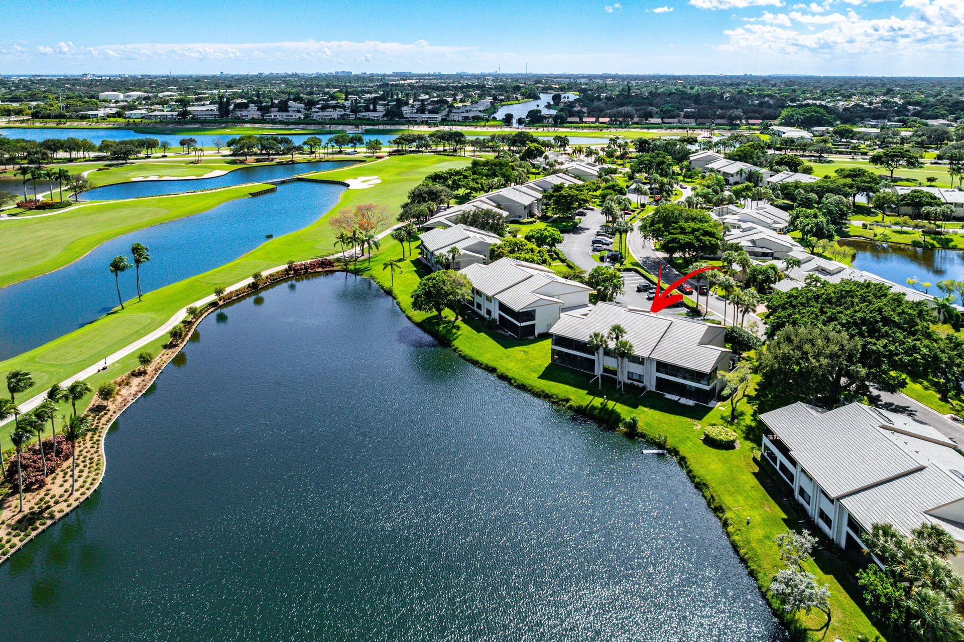 Aerial perspective of a multi-story building featuring a hipped roof, situated on a waterfront lot with grass lawns, mature landscaping, and proximity to a golf course