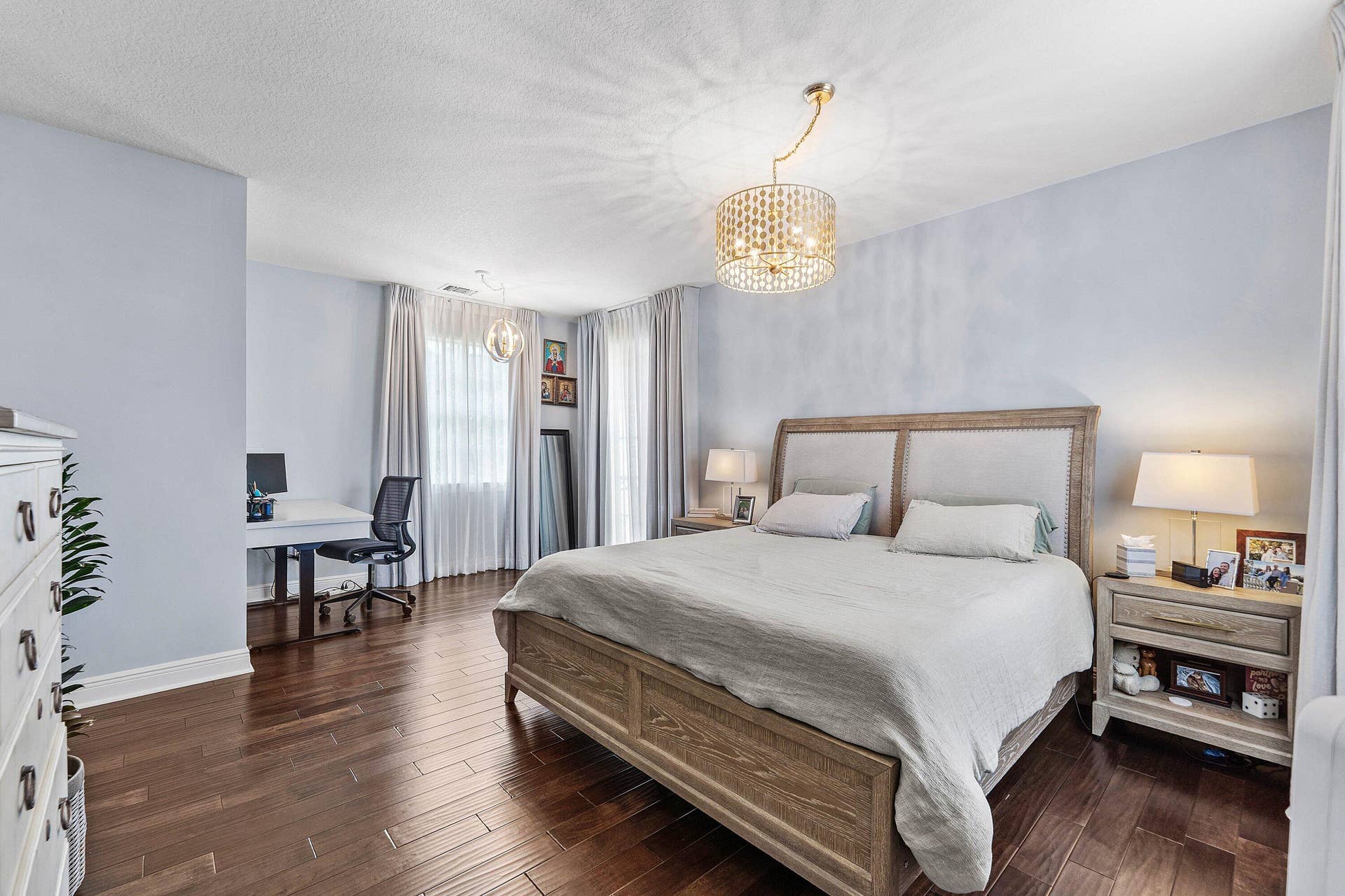 115 VIA POINCIANA Lane, Boca Raton, FL 33487 Spacious master bedroom with rich wood flooring, elegant lighting, abundant natural light, and a stylish sitting area.