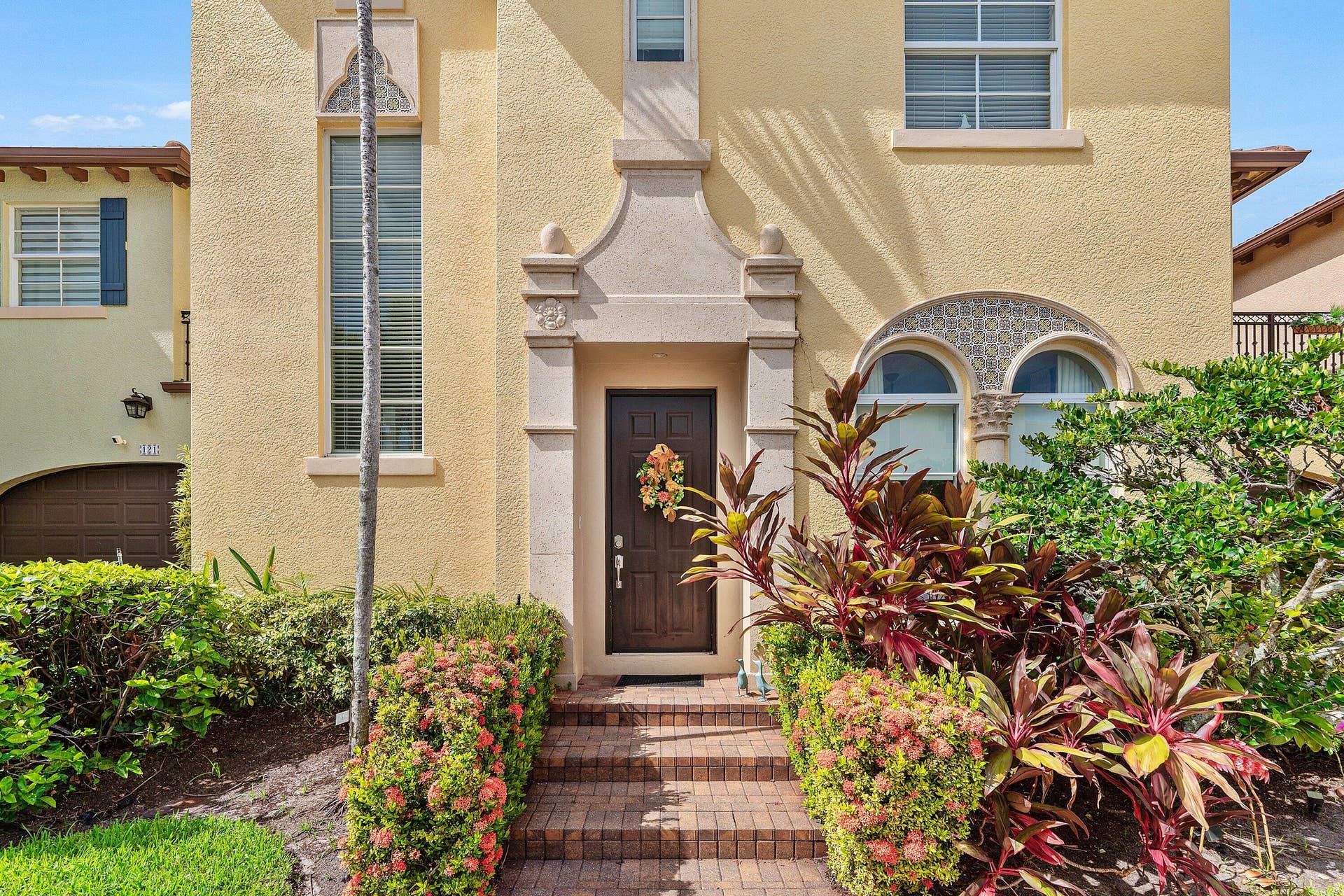 115 VIA POINCIANA Lane, Boca Raton, FL 33487 Welcoming front entry featuring an elegant arched doorway, decorative architectural details, and tropical landscaping.