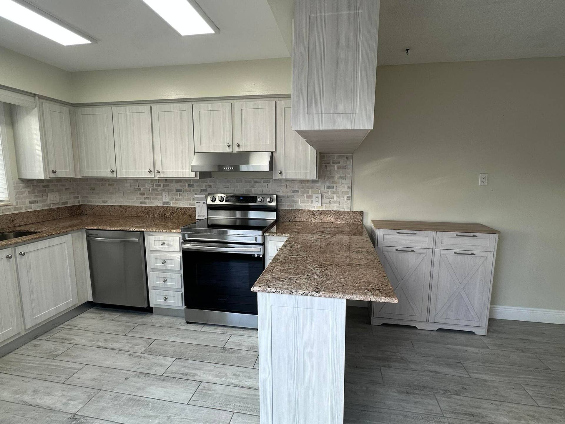 Kitchen featuring light-finish cabinetry, stone-texture countertops, stainless steel appliances, a subway-style tiled backsplash, and wood-finish tile flooring