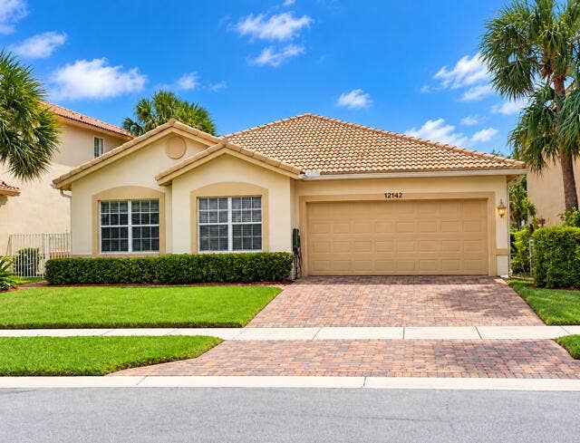 12142 Colony Preserve Drive, Boynton Beach, FL 33436 Charming single-story home featuring a Spanish tile roof, brick paver driveway, attached 2-car garage, and manicured tropical landscaping.