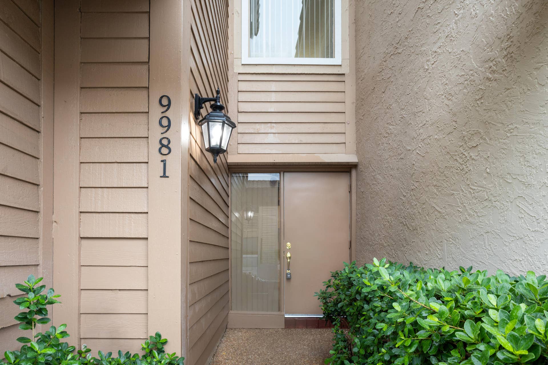9981 W ATLANTIC Boulevard, #9981, Coral Springs, FL 33071 Welcoming entry featuring horizontal siding exterior, illuminated wall sconce, brushed metal door hardware, and lush green landscaping with mature shrubs flanking the entrance