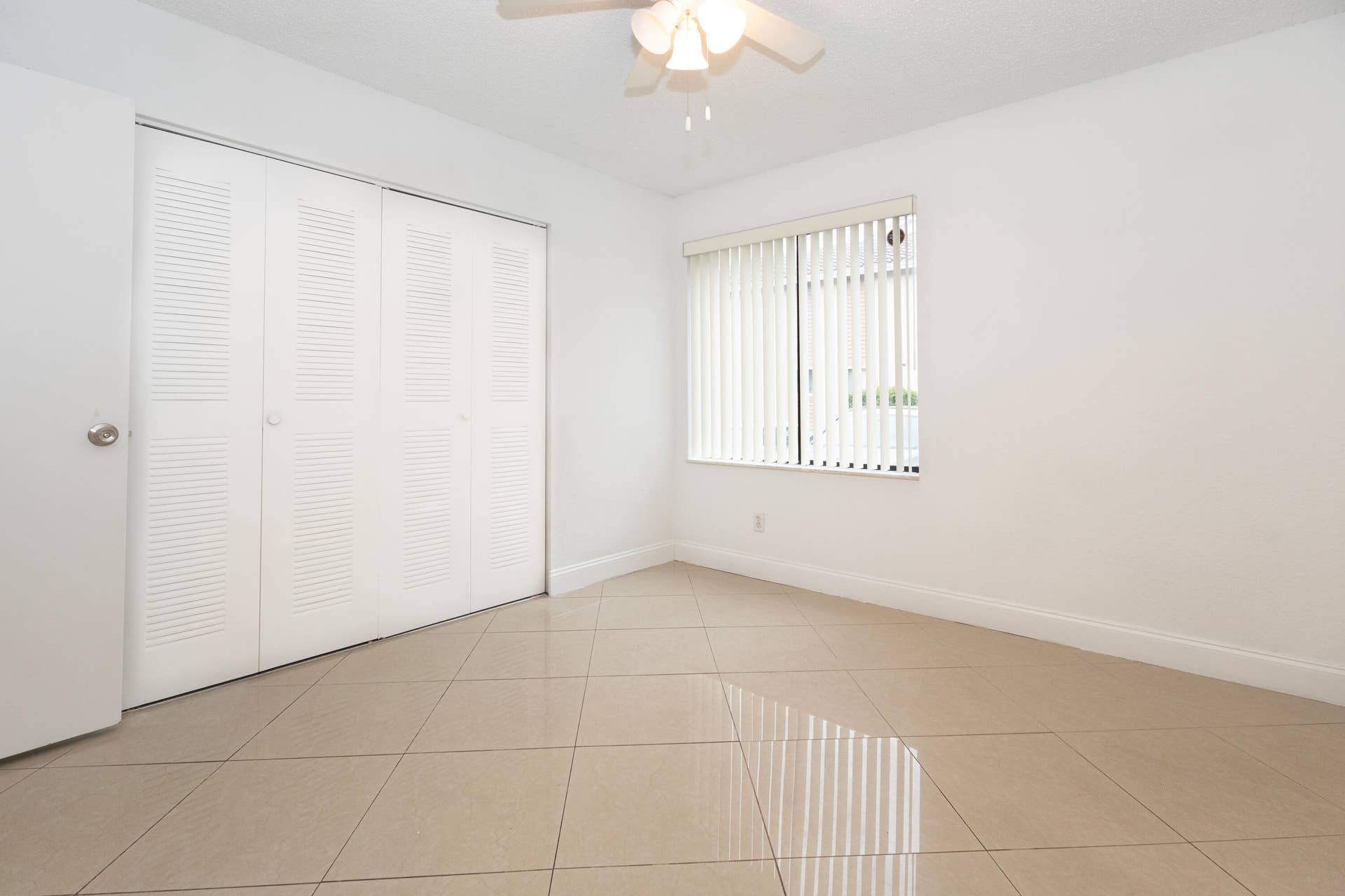 9981 W ATLANTIC Boulevard, #9981, Coral Springs, FL 33071 Bright and spacious room featuring tile flooring, a ceiling fan with integrated lighting, louvered closet doors, and large windows with vertical blinds allowing ample natural light