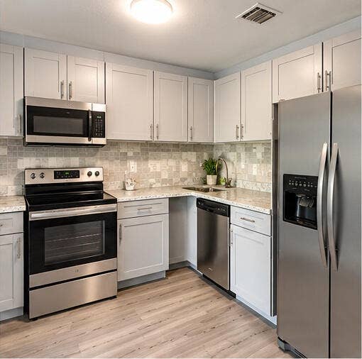3601 SW 54th Avenue, West Park, FL 33023 Kitchen featuring shaker-style cabinetry, stainless steel appliances, speckled stone-finish countertops, tile backsplash, and wood-finish flooring