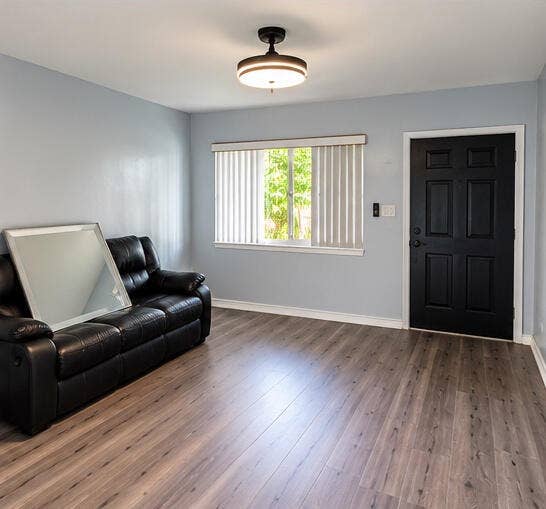 3601 SW 54th Avenue, West Park, FL 33023 Wood-finish flooring, matte black entry door, semi-flush mount drum light fixture, and horizontal window with vertical blinds