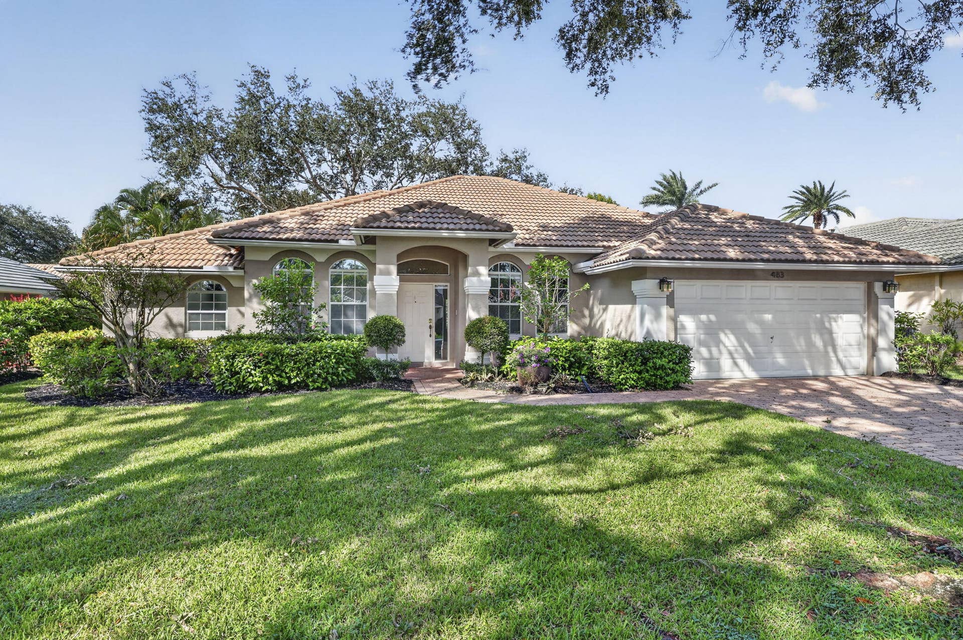 483 OTTER Lane N, Jupiter, FL 33458 Single-story residence featuring a tile roof, arched windows, covered entryway, and a brick-paver driveway