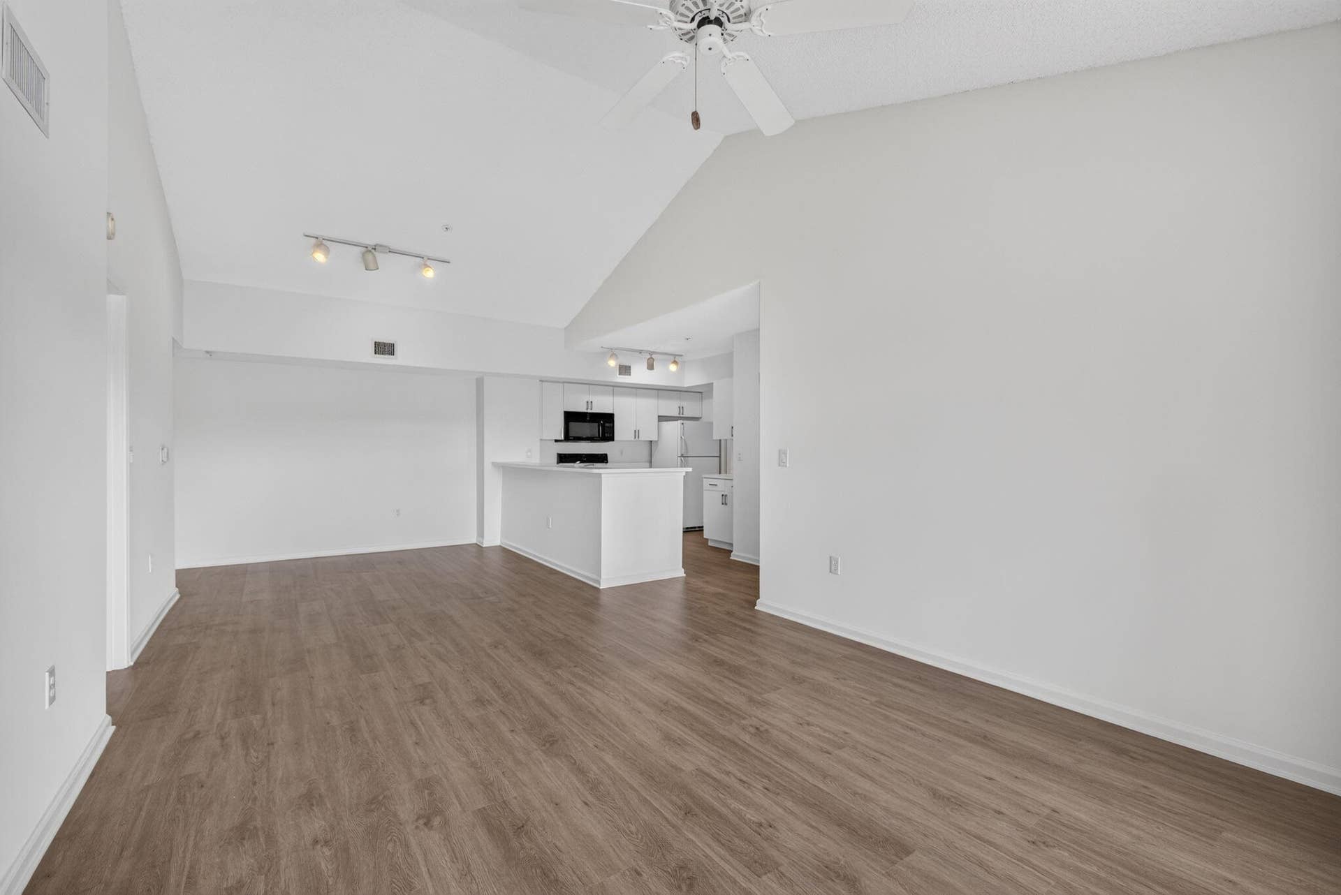 Vaulted ceilings, vinyl plank flooring, kitchen island with breakfast bar, track lighting, and a ceiling fan