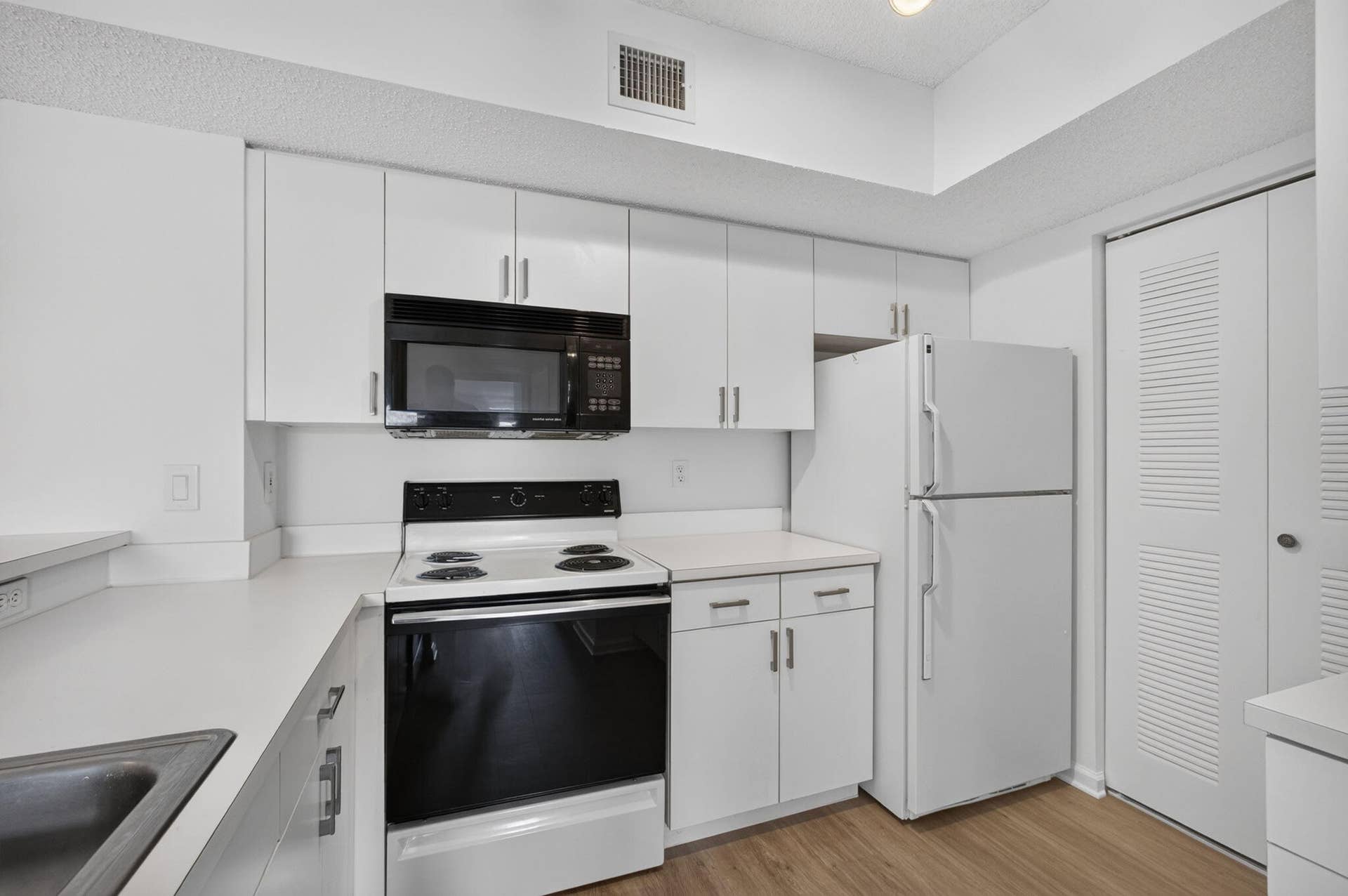 Kitchen featuring white cabinetry, solid-surface countertops, vinyl plank flooring, and built-in appliances including a microwave, range, and refrigerator.