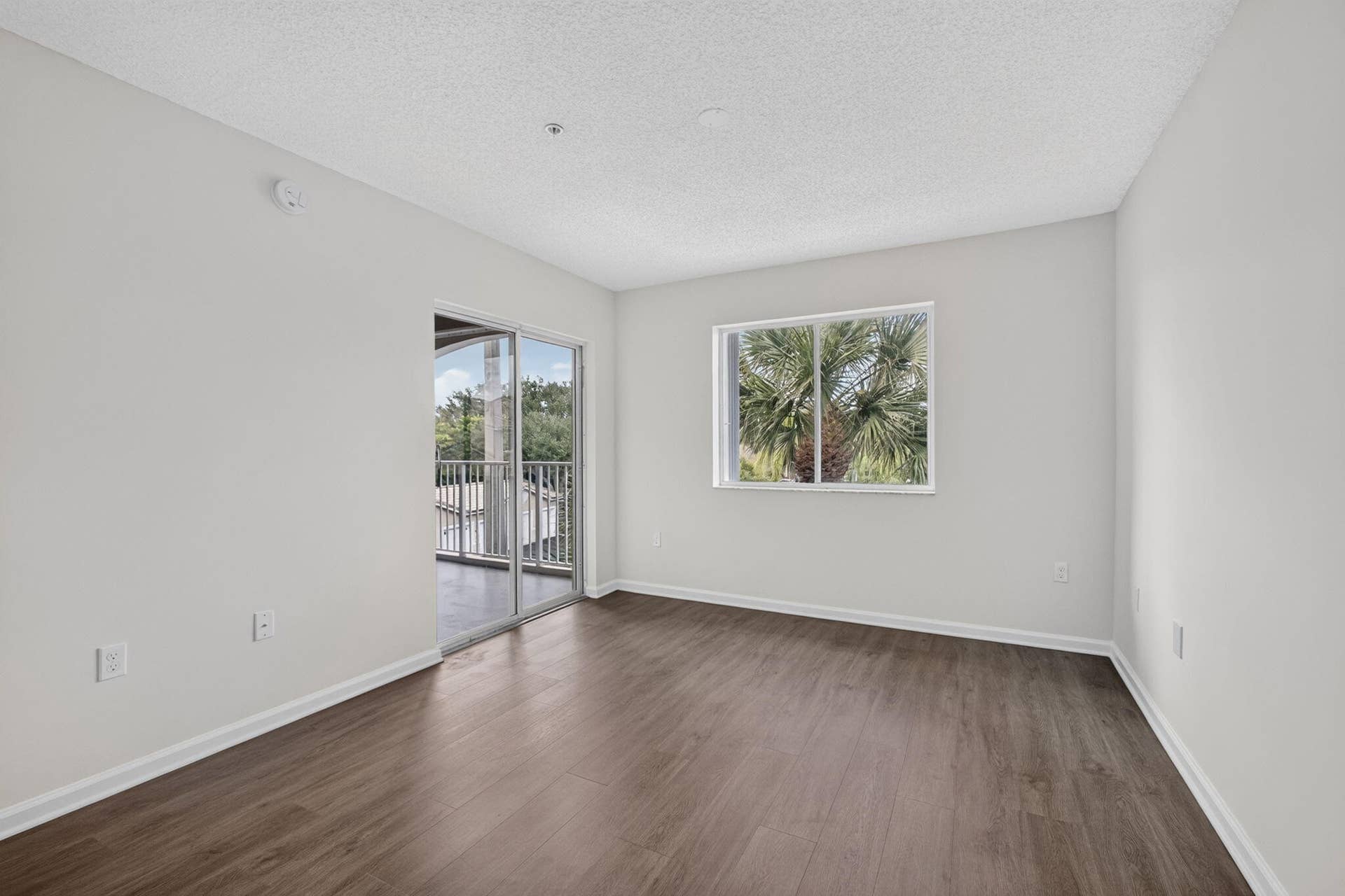 Neutral-toned interior featuring vinyl plank flooring, sliding glass door, leading to balcony and a horizontal window
