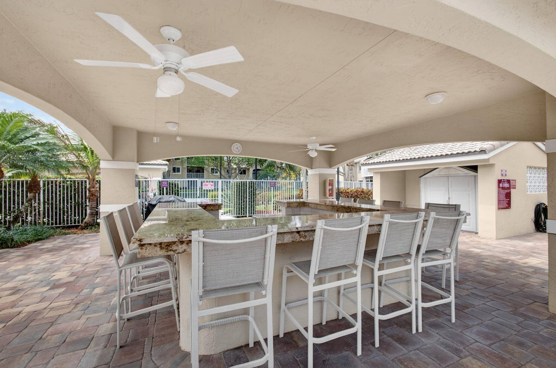 Covered outdoor bar area featuring a stone-topped bar, paver patio flooring, and overhead ceiling fans