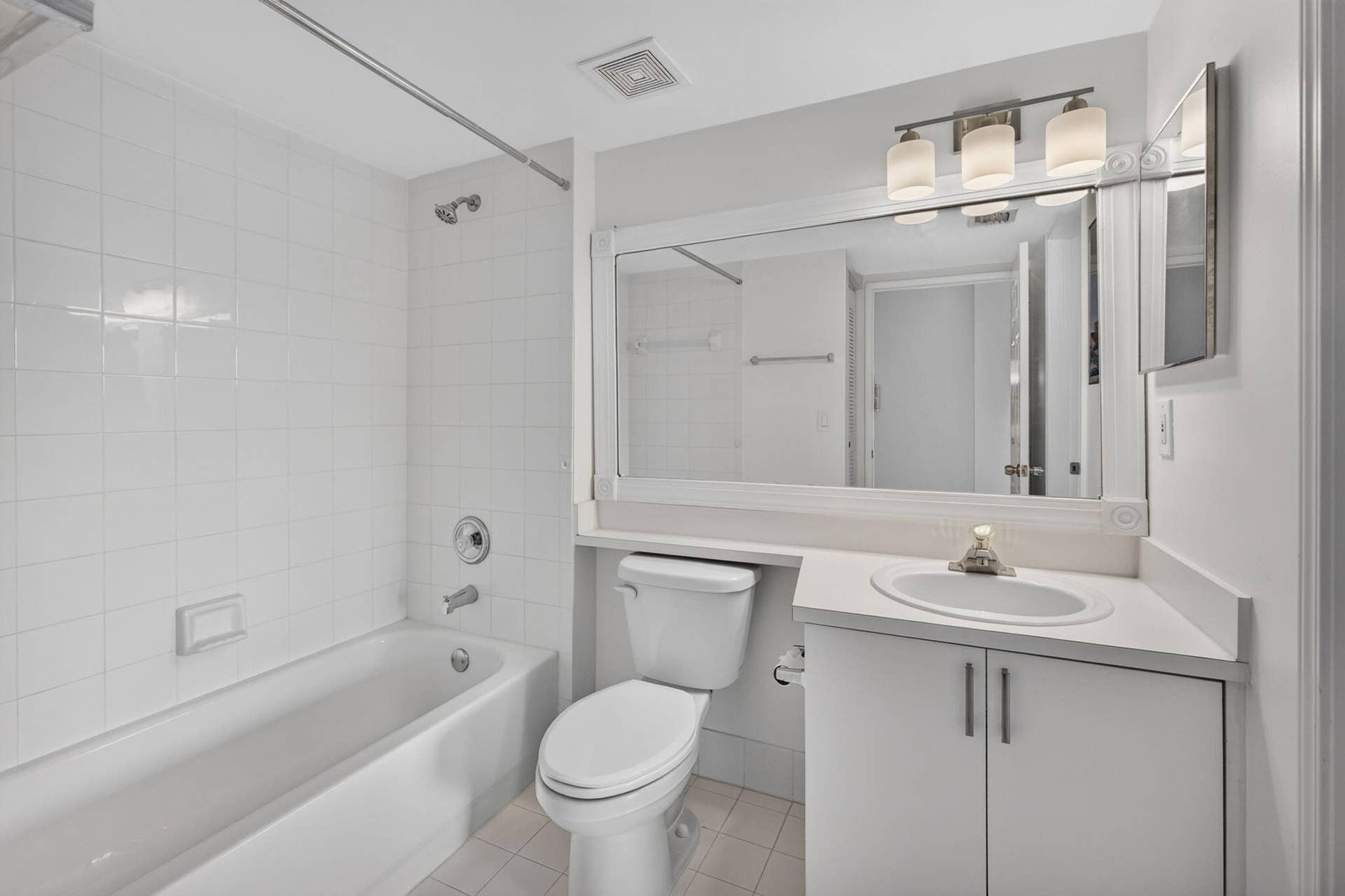 Bathroom featuring a tub-shower combination with floor-to-ceiling tile surround, white cabinetry, integrated sink with countertop, oversized wall-mounted mirror, and three-light fixture