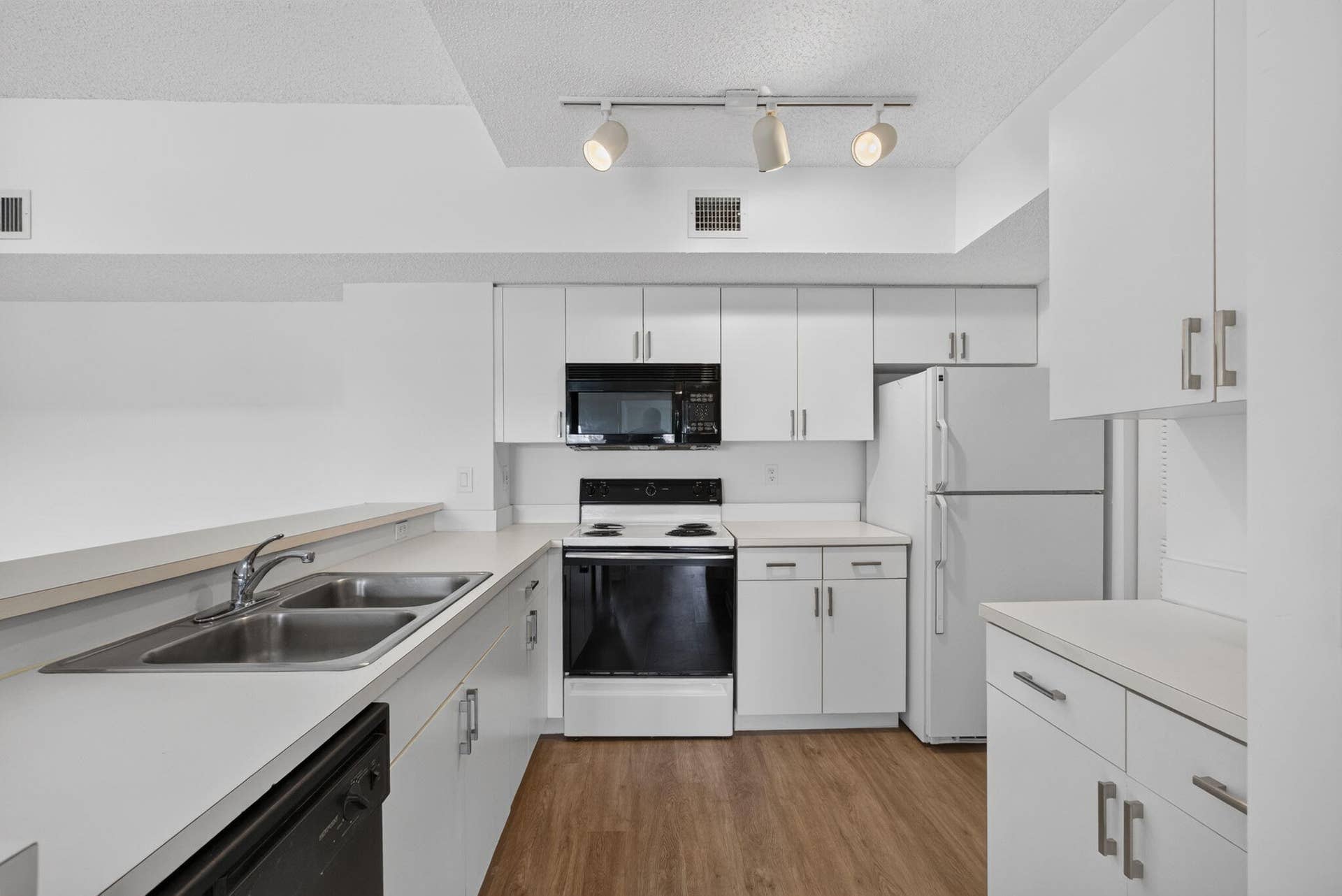 Kitchen featuring white cabinetry, vinyl plank flooring, a double-basin stainless steel sink, black appliances and adjustable track lighting.