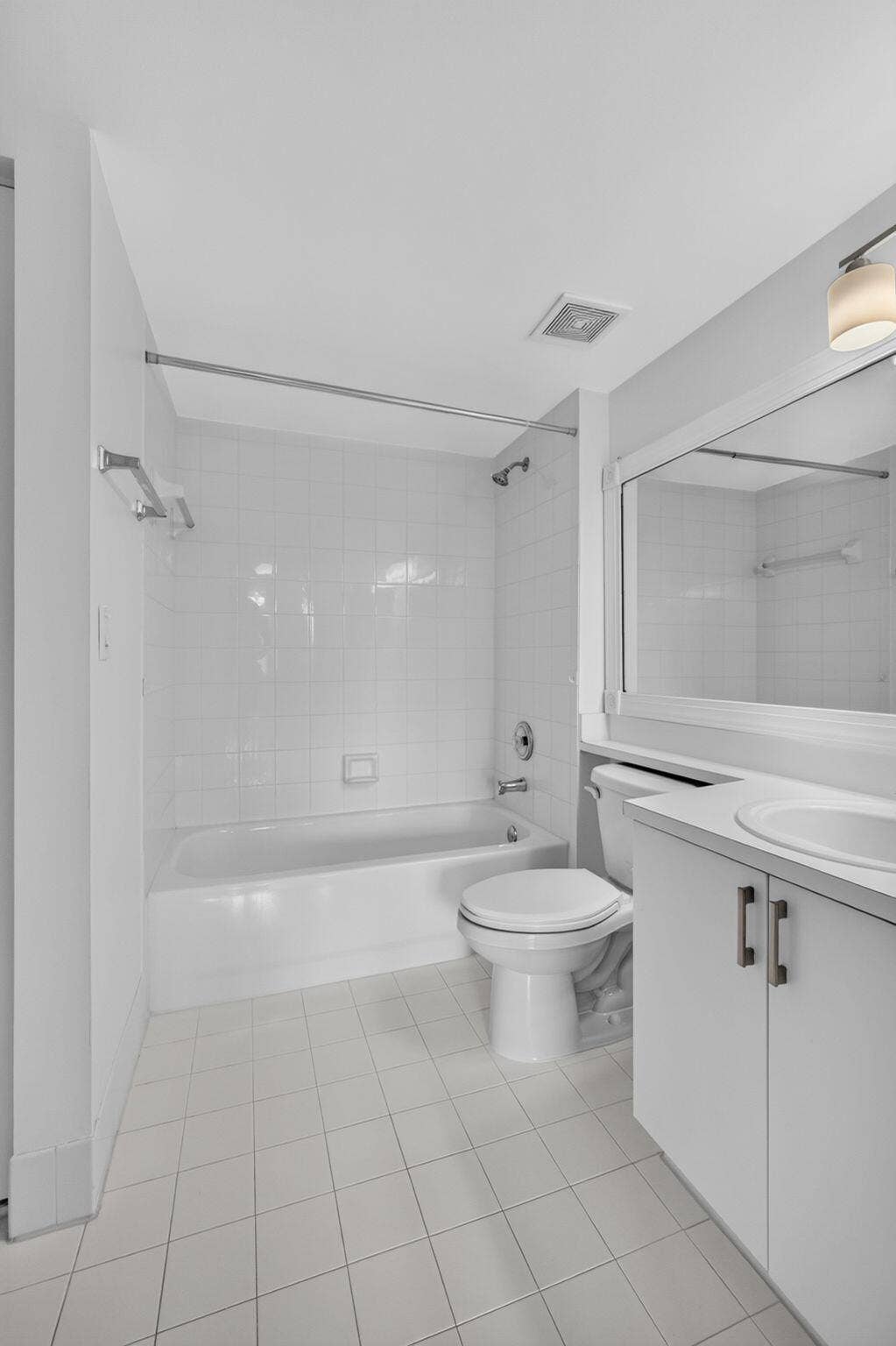 Bathroom featuring white tile flooring, a tub-shower combination with floor-to-ceiling tile surround, a built-in vanity with a solid-surface countertop, and an oversized wall-mounted mirror