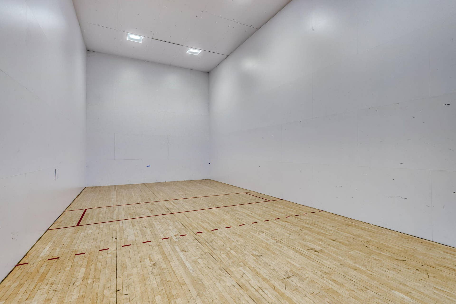 Indoor court featuring wood-finish flooring, high-impact paneled walls, and recessed ceiling lighting