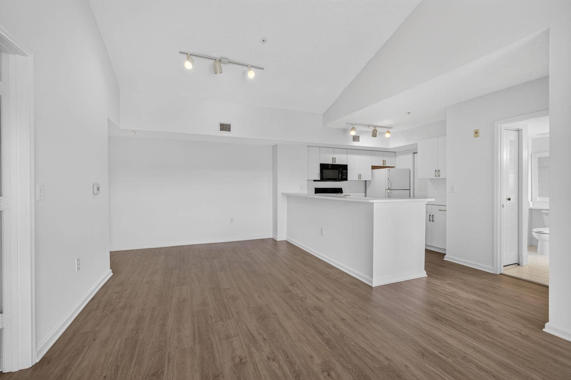 Open-concept interior featuring vaulted ceilings, vinyl plank flooring, white cabinetry, a breakfast bar, and adjustable track lighting.