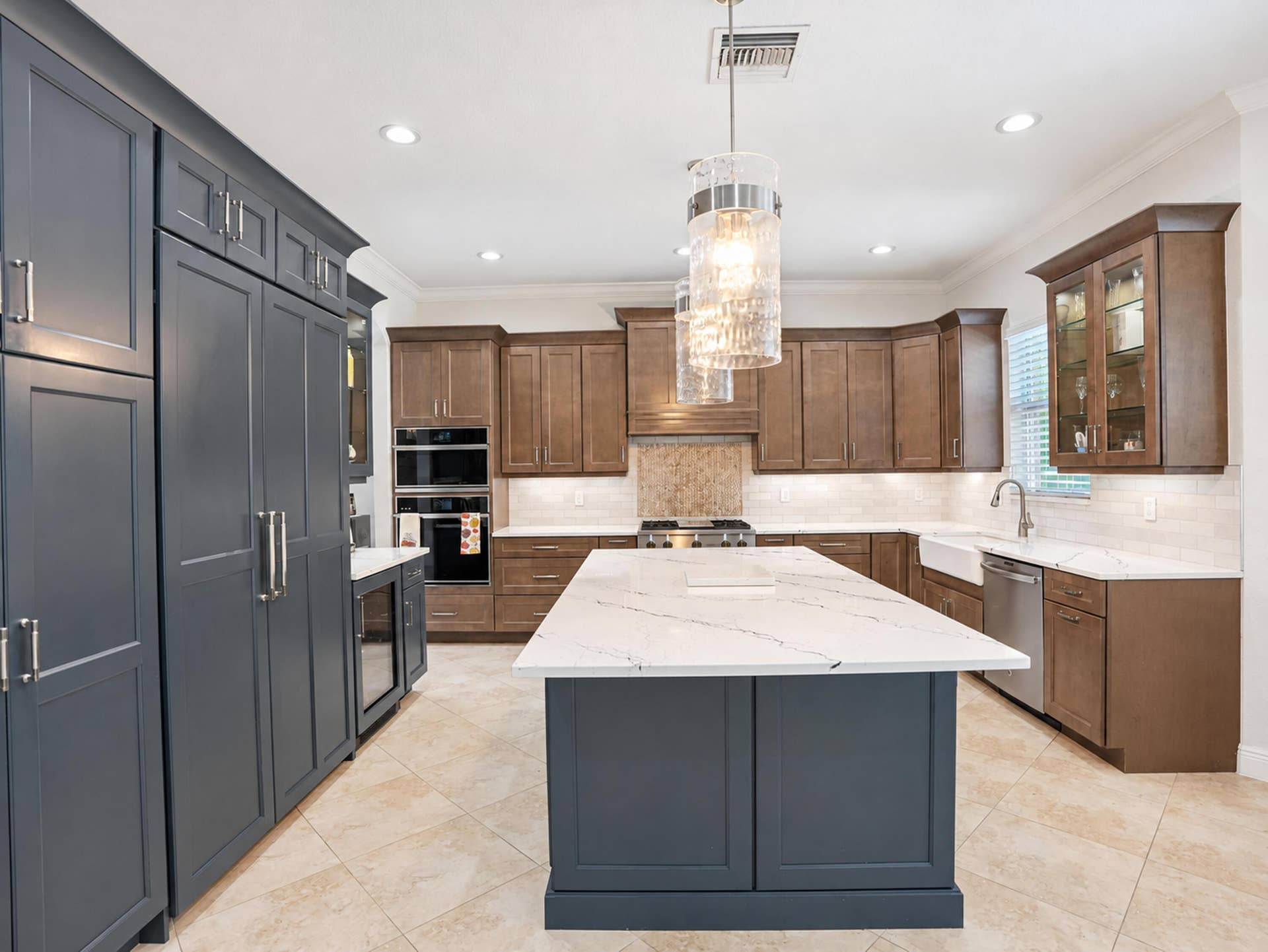 8601 Waterside Court, Parkland, FL 33076 Kitchen featuring an oversized central island with stone-finish countertops, custom two-toned cabinetry, dual built-in wall ovens, porcelain farmhouse sink, and polished glass-paneled pendant lighting