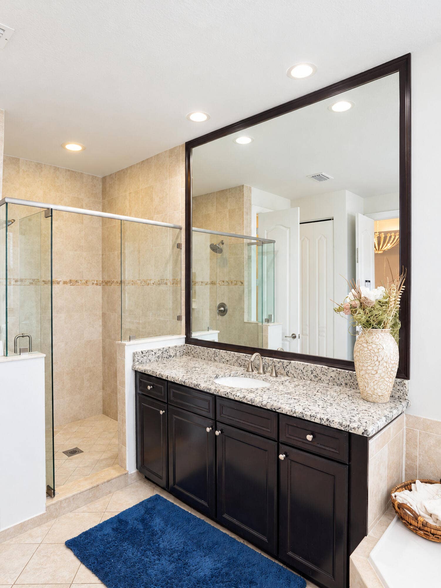 8601 Waterside Court, Parkland, FL 33076 Bathroom vanity with dark cabinetry, stone-surface countertop, oval undermount sink, large framed mirror, and tiled walk-in shower with glass enclosure