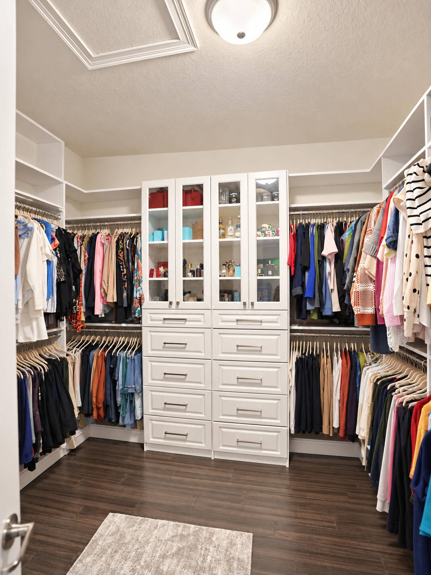 8601 Waterside Court, Parkland, FL 33076 Walk-in closet featuring white built-in cabinetry with glass-front display uppers, stacked storage drawers, wood-finish flooring, and multi-tier hanging rods