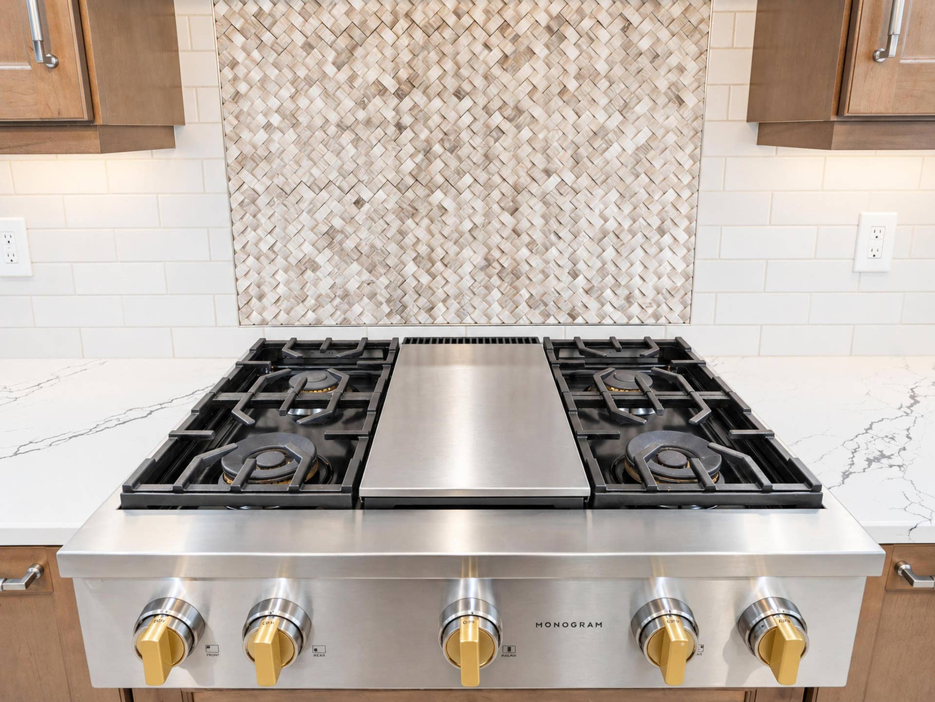 8601 Waterside Court, Parkland, FL 33076 Stainless steel professional-grade gas range with central griddle, light-toned stone-finish countertops, custom herringbone-patterned tile backsplash, and wood-finish cabinetry