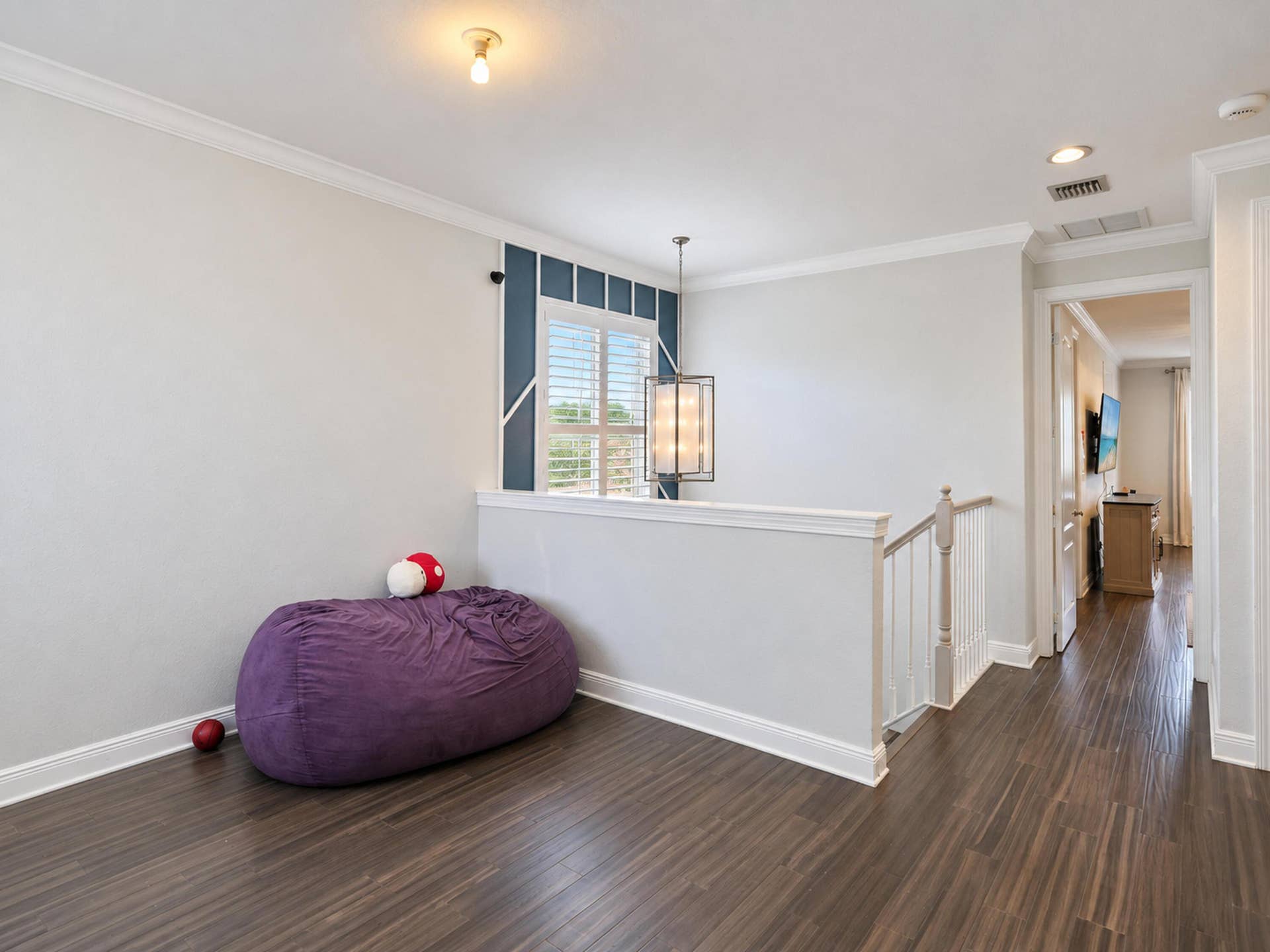8601 Waterside Court, Parkland, FL 33076 Interior space featuring wood-finish flooring, crown molding, a hanging pendant light fixture, plantation shutters, and a stairwell with a painted wood balustrade