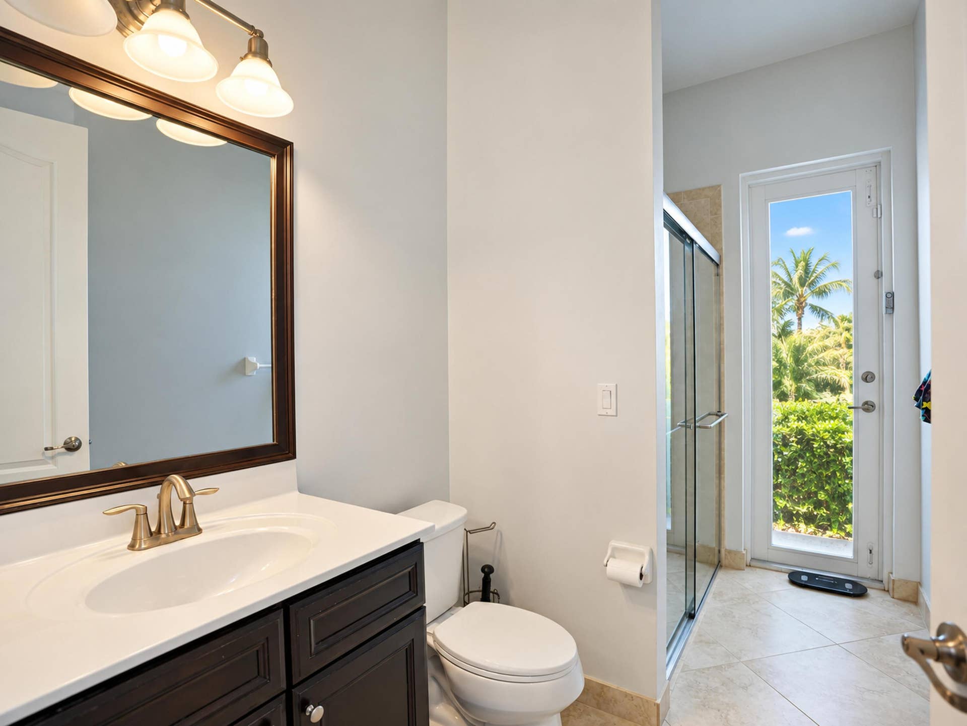 8601 Waterside Court, Parkland, FL 33076 Dark wood-finish vanity with a white countertop and oval undermount sink, framed mirror with integrated vanity lighting, glass-enclosed shower, and full-glass door exterior access