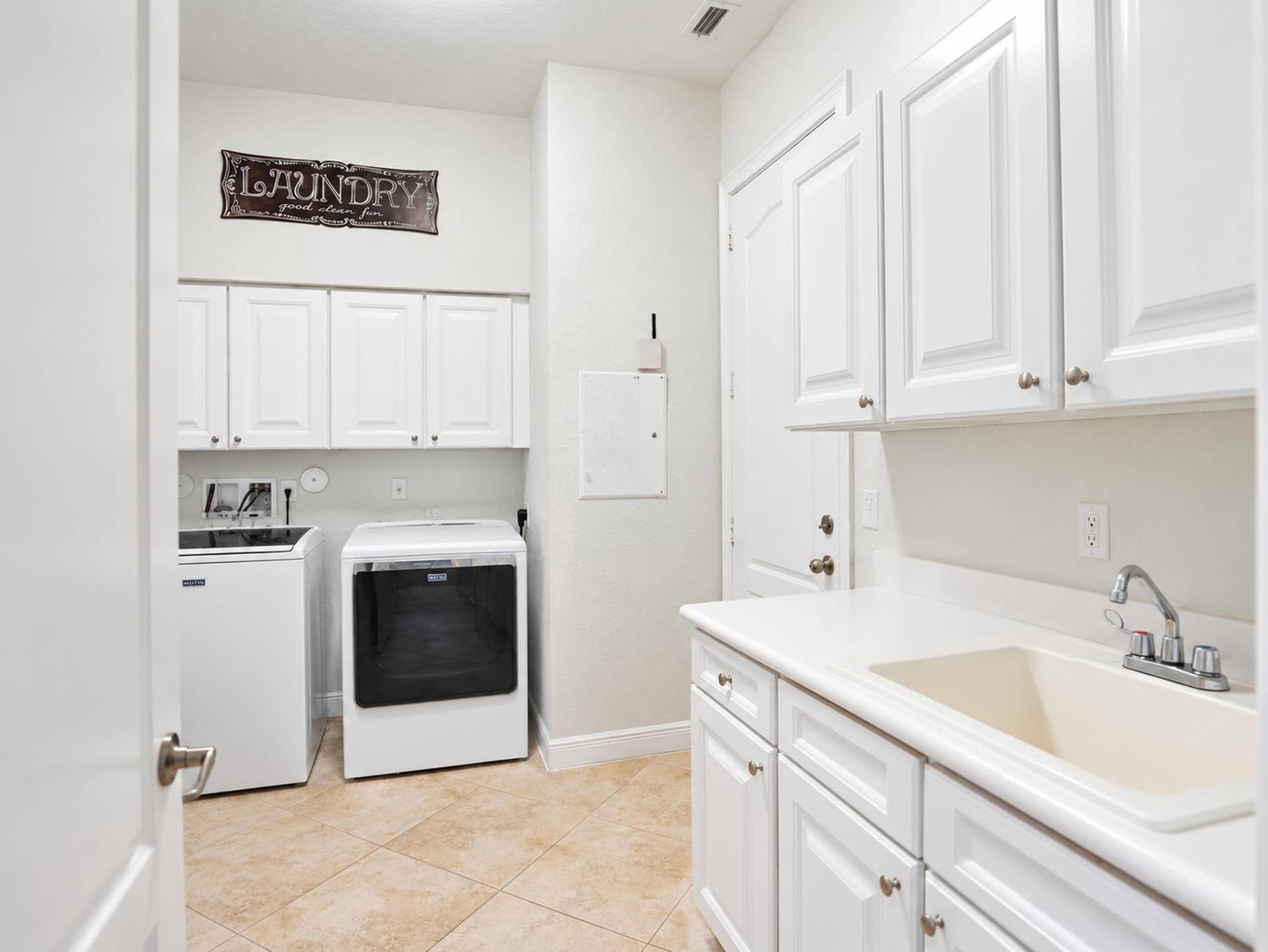 8601 Waterside Court, Parkland, FL 33076 Laundry room featuring white cabinetry, stone-finish tile flooring, a built-in utility sink with a chrome faucet, and ample wall-mounted storage cabinets